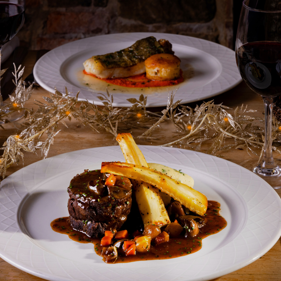 Elegant holiday dining table setting with gourmet beef dish, roasted vegetables, wine glasses, and festive decorations