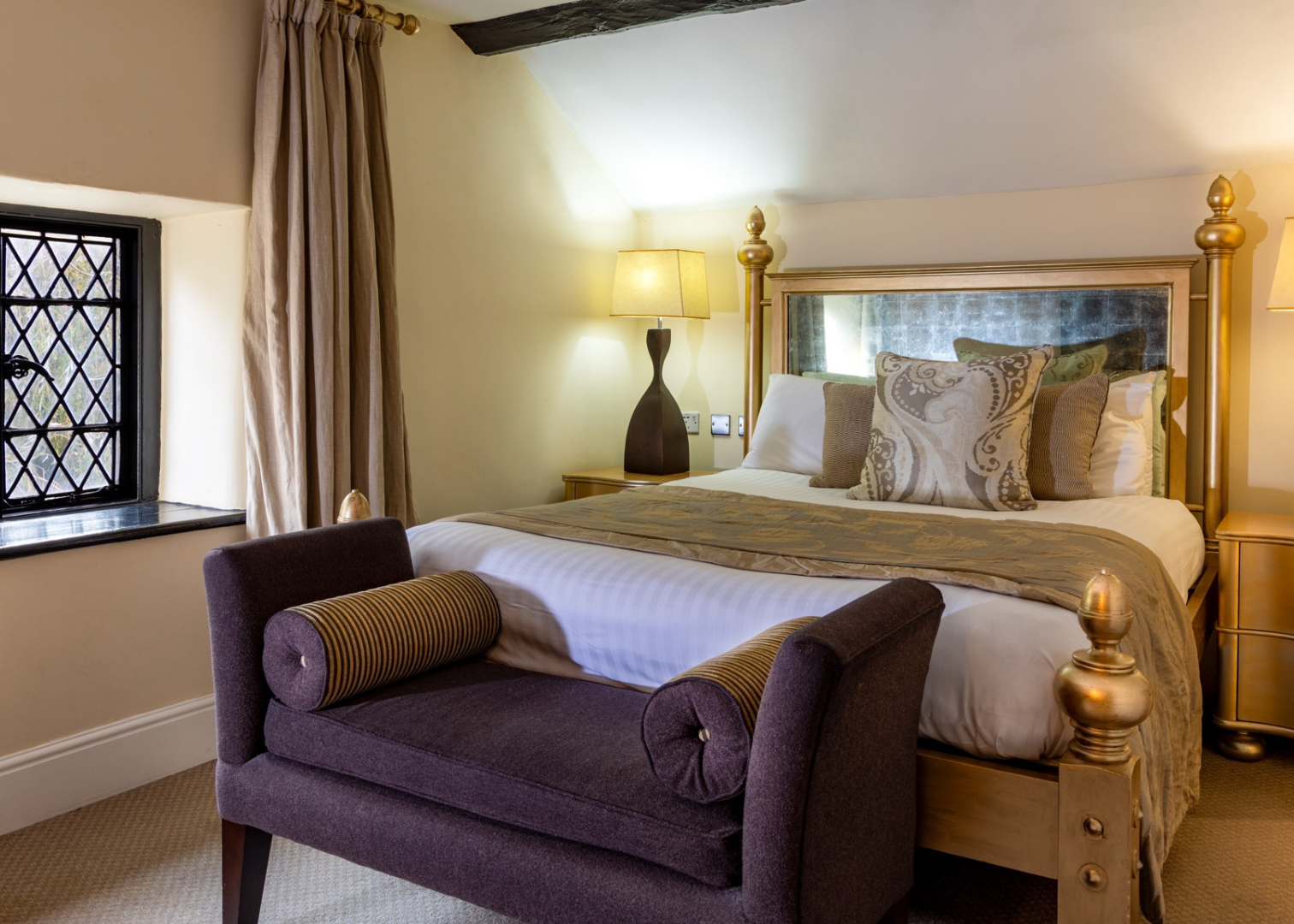 Elegant bedroom with gold accents, purple bench, and decorative pillows