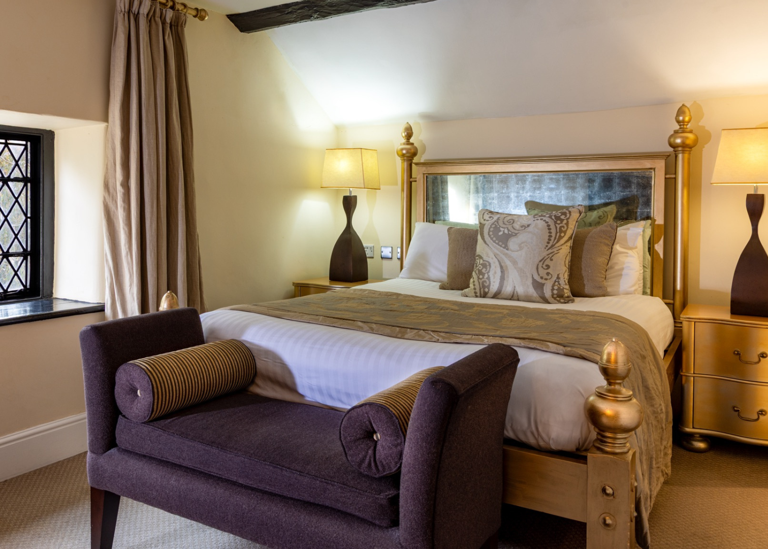 Elegant bedroom with gold accents, purple bench, and decorative pillows