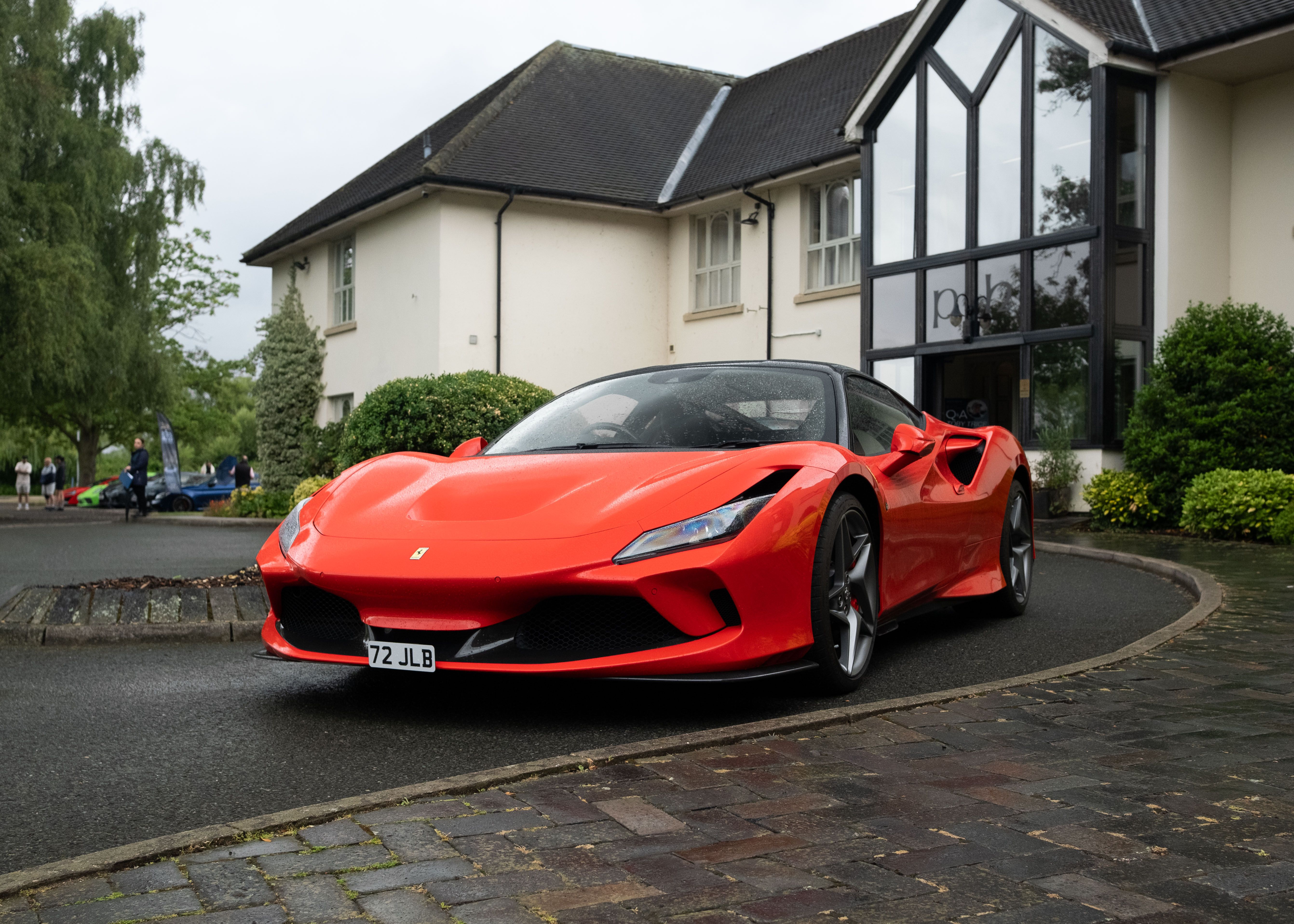 A red Ferrari sports car parked in front of a modern building on a cloudy day.