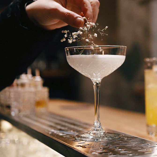 Hand placing flowers on a cocktail glass with a white drink