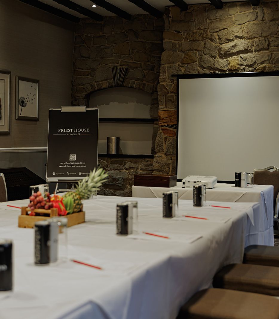 Conference room with a large table, chairs, projector, and screen at Priest House by the River