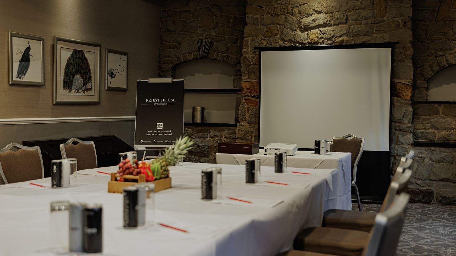 Conference room with a large table, chairs, projector, and screen at Priest House by the River
