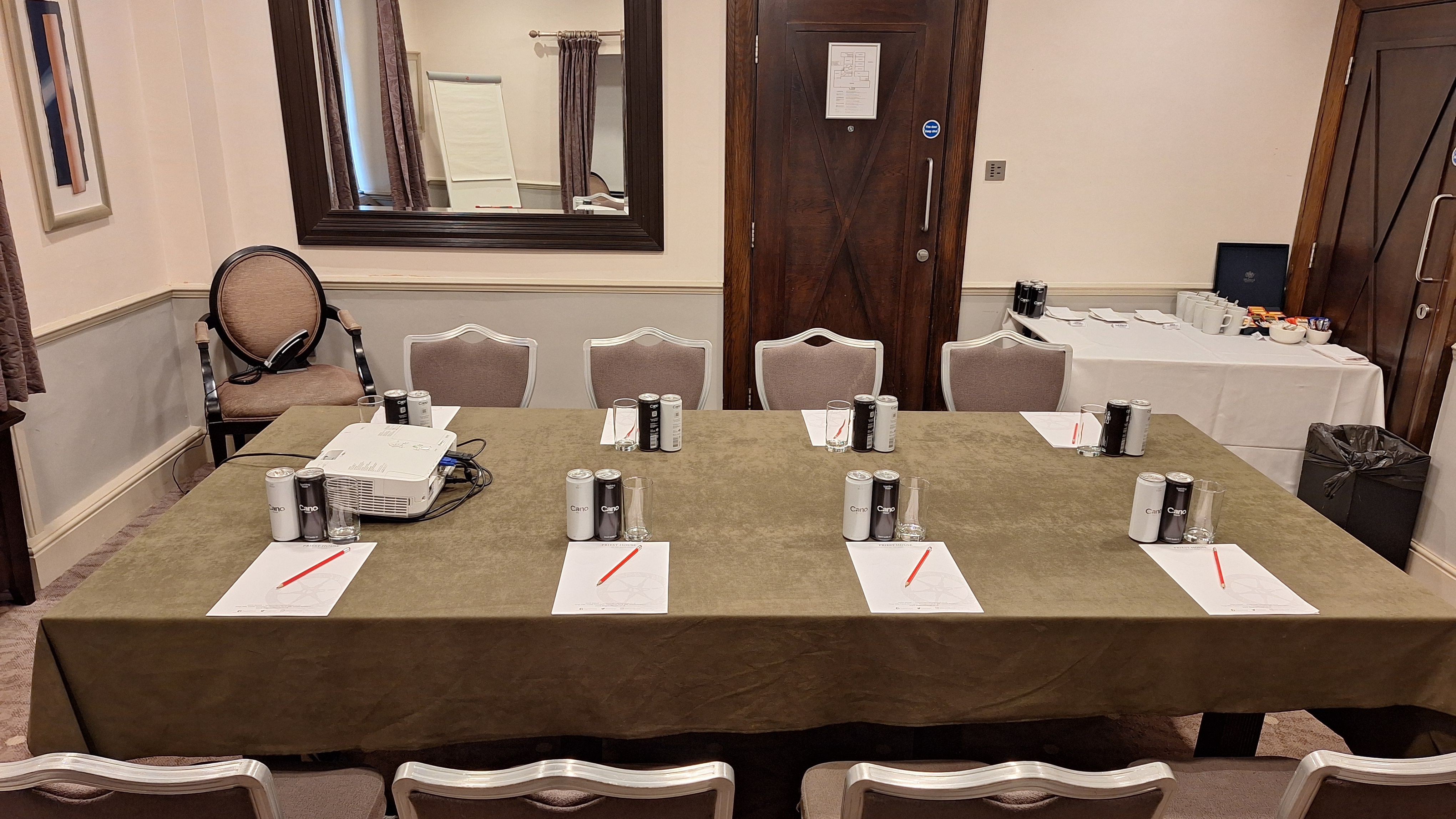 A meeting room with a table set for a conference, including notepads, pens, drinks, and a projector.