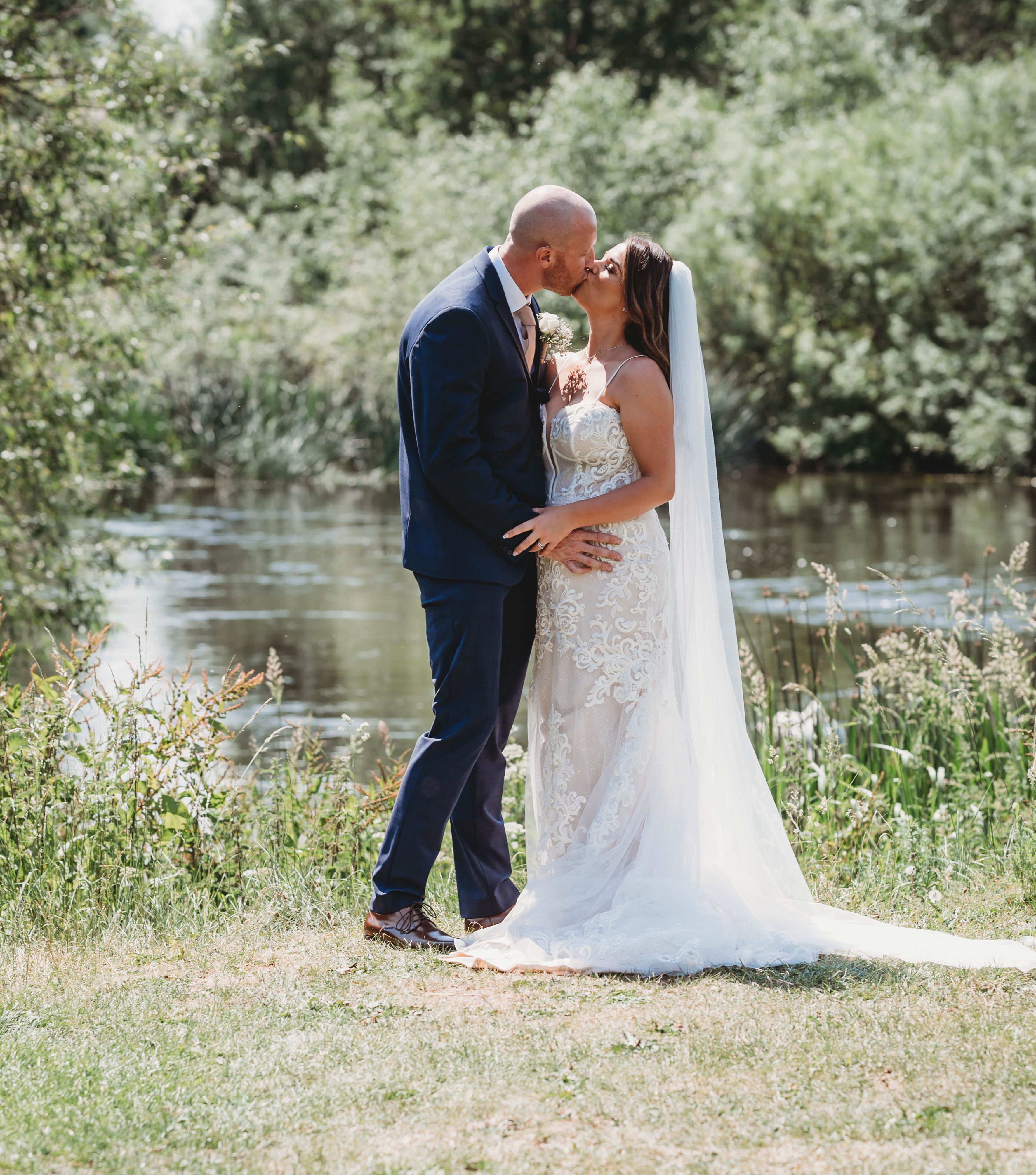 Bride and groom kissing outdoors beside a pond