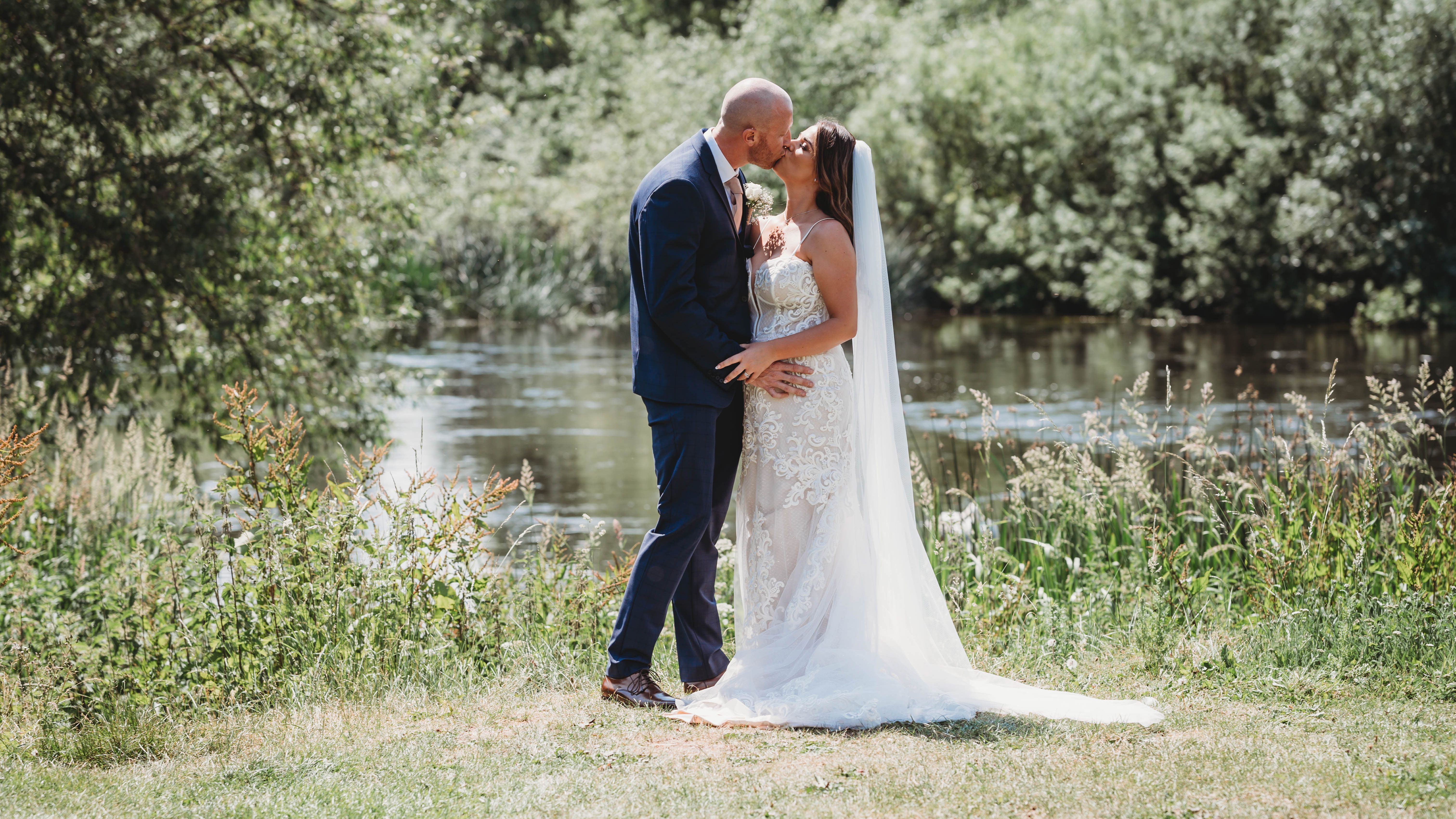 Bride and groom kissing outdoors beside a pond