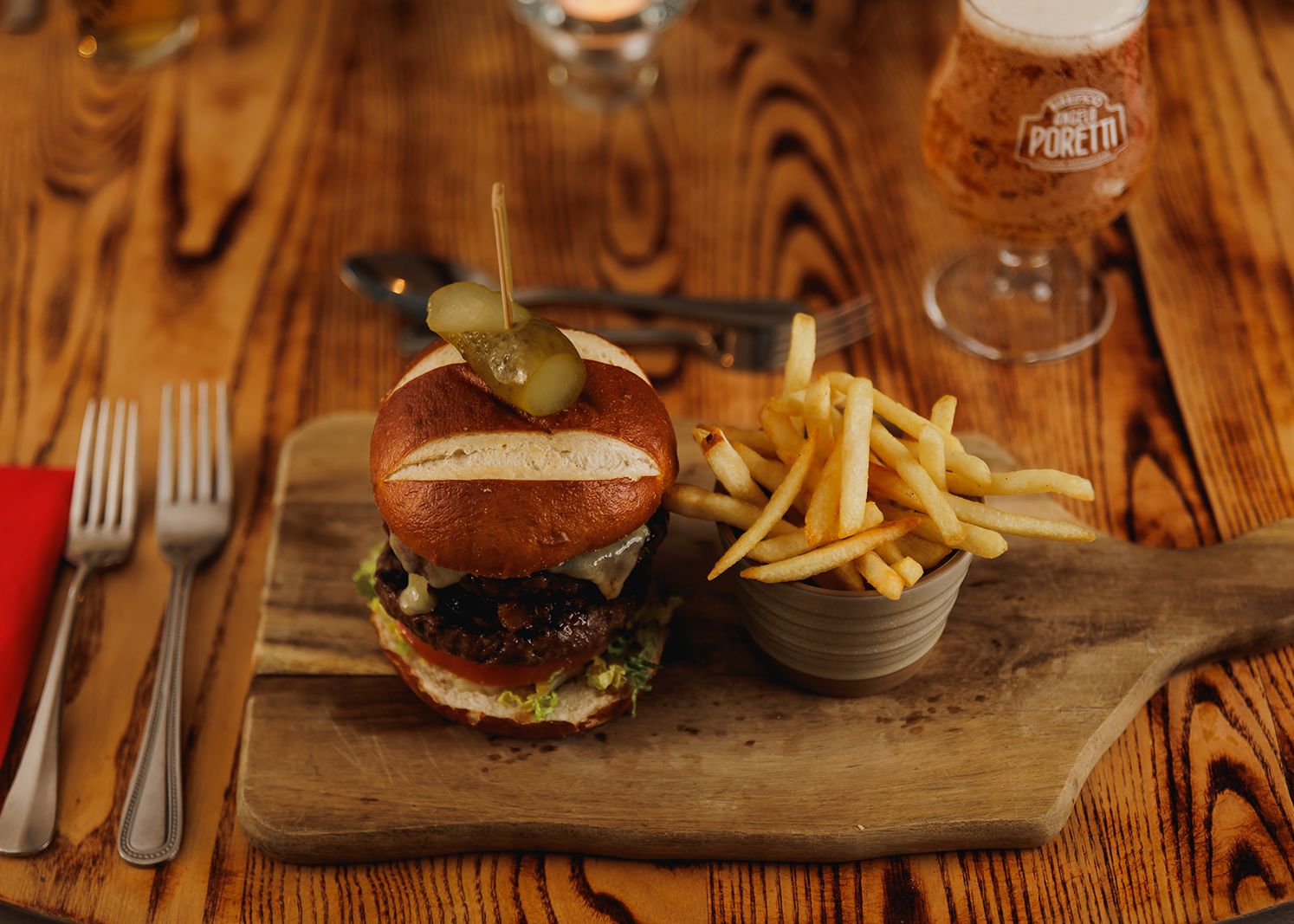 Burger with French fries served on a wooden board next to a glass of beer