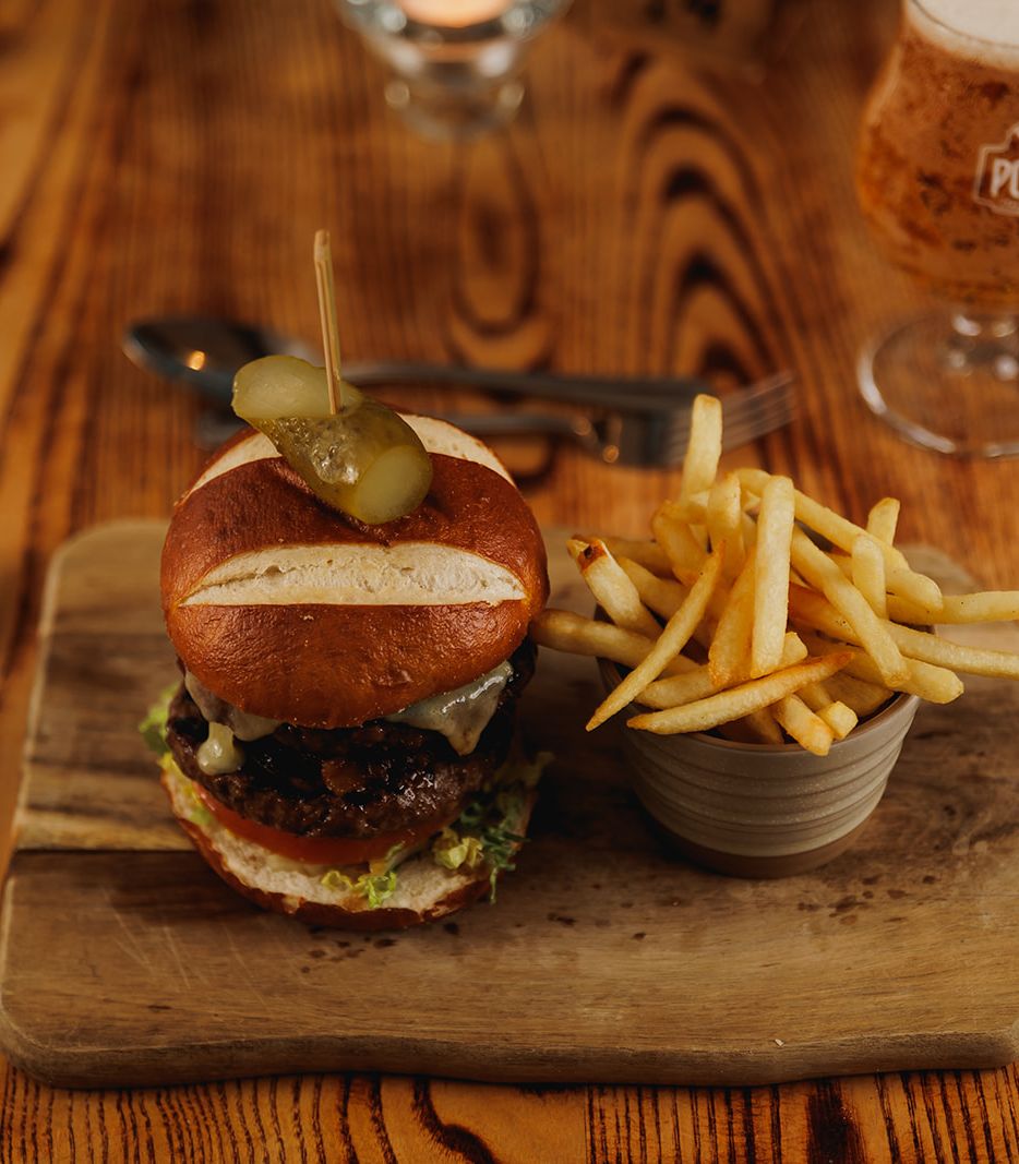 Burger with French fries served on a wooden board next to a glass of beer
