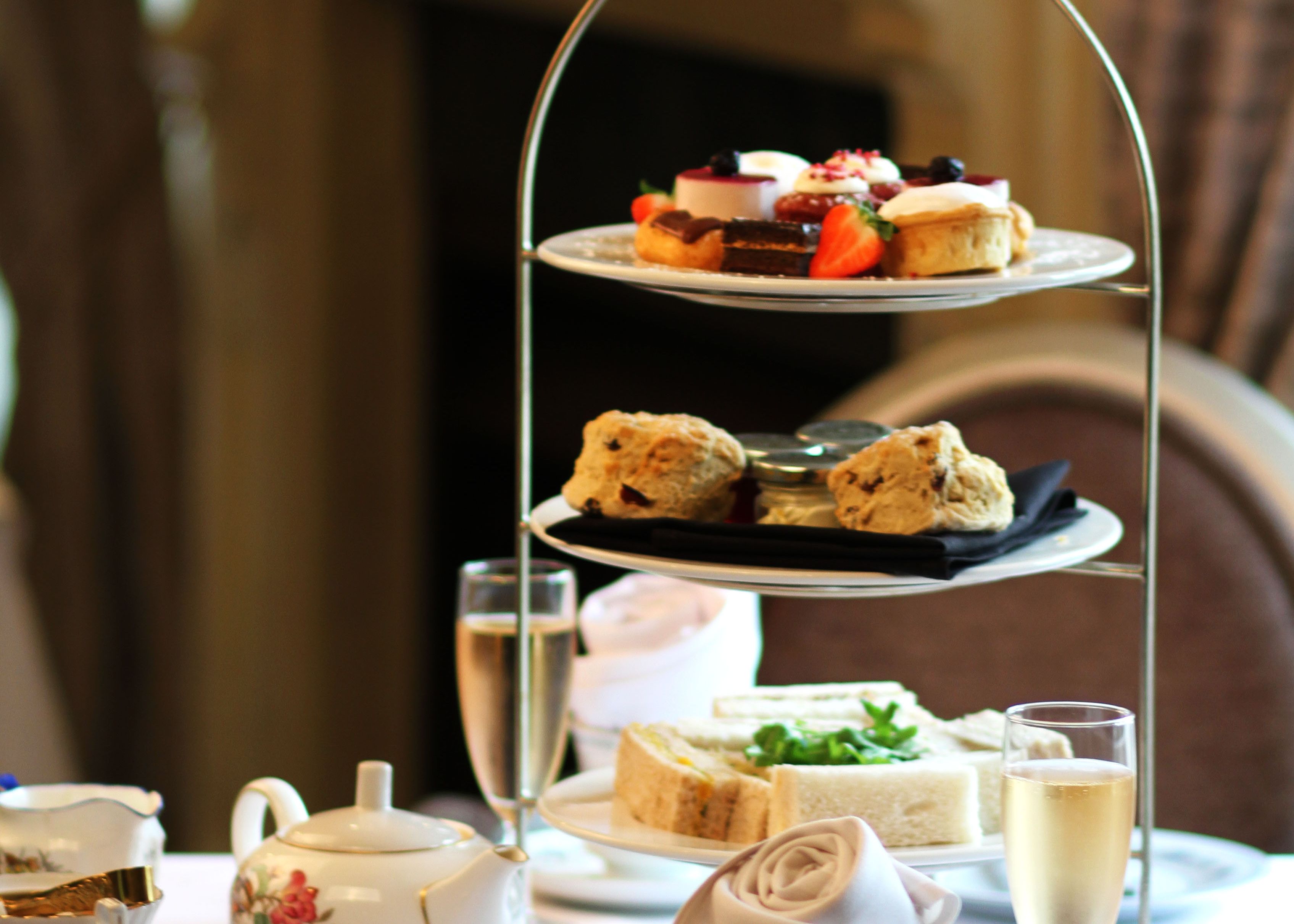 Traditional afternoon tea set with three-tiered tray of sweets, scones, and sandwiches, teapot, cups, and champagne glasses.