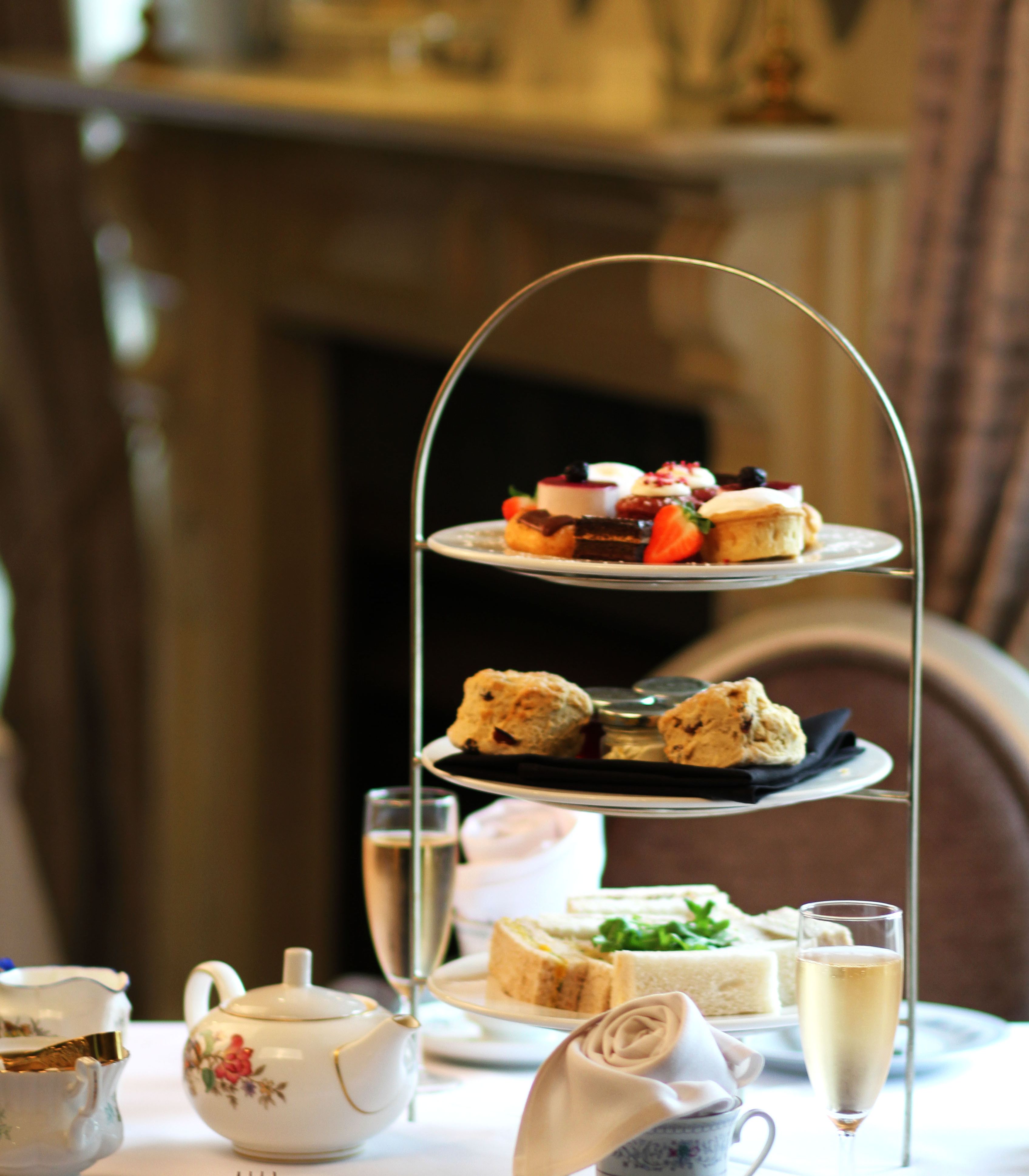 Traditional afternoon tea set with three-tiered tray of sweets, scones, and sandwiches, teapot, cups, and champagne glasses.