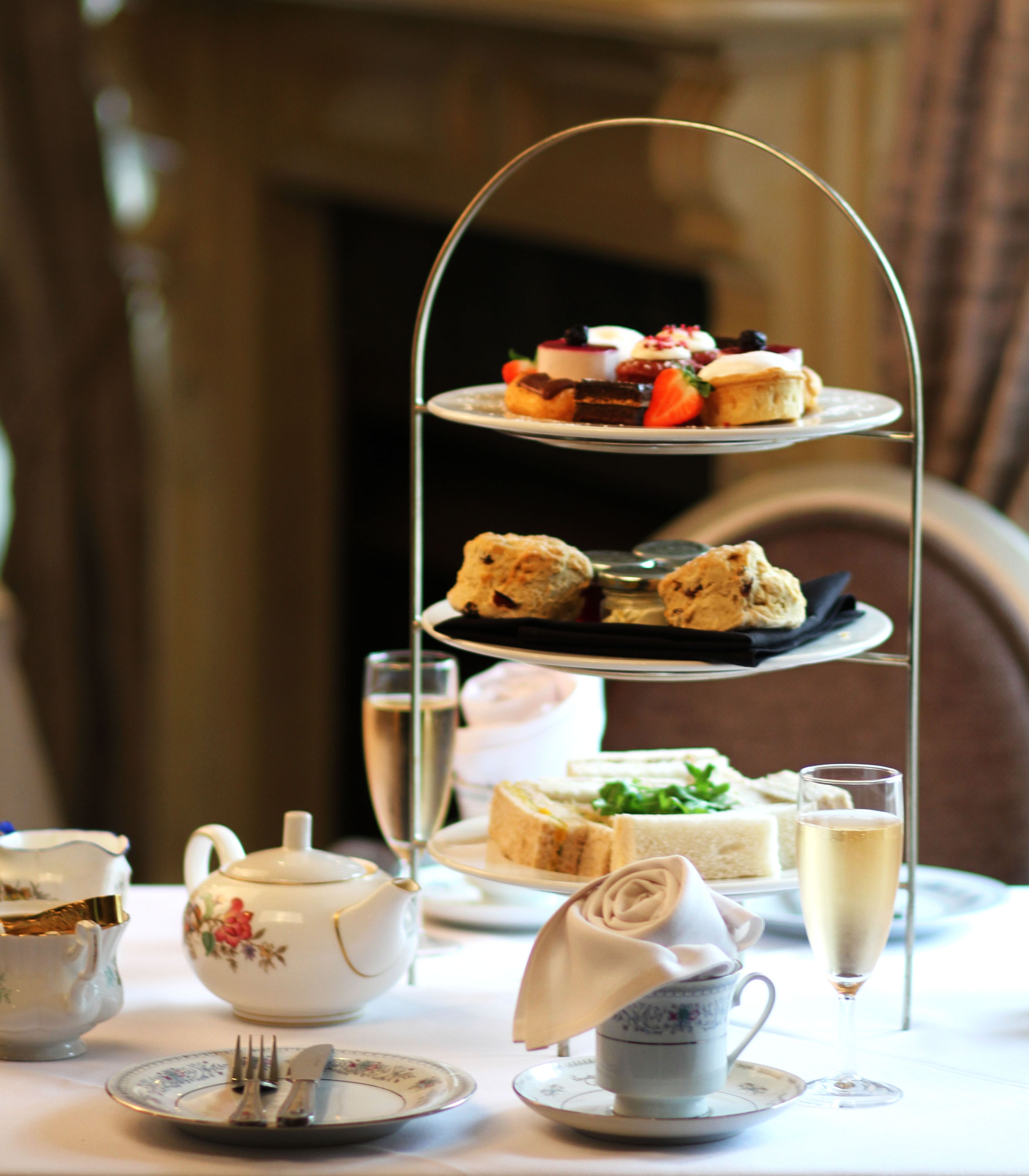 Traditional afternoon tea set with three-tiered tray of sweets, scones, and sandwiches, teapot, cups, and champagne glasses.