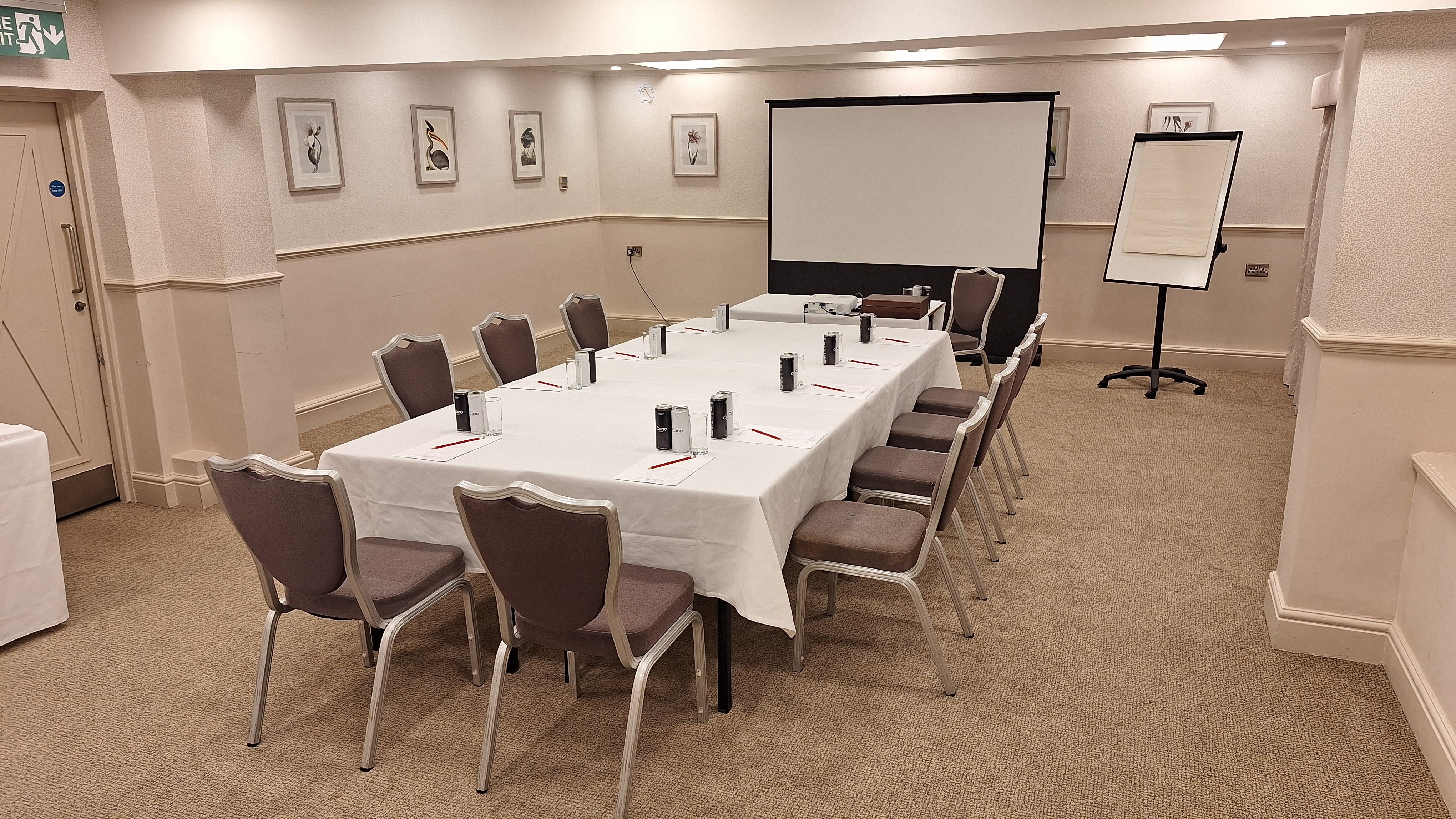 Conference room setup with a rectangular table, chairs, projector screen, and flipchart