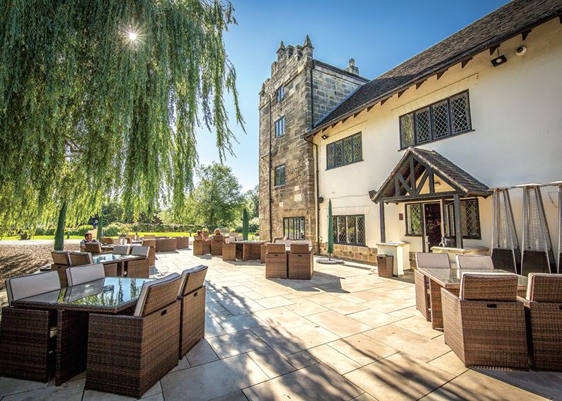 Outdoor seating area of a historic building with wicker furniture and lush landscaping