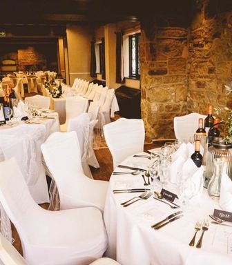 Elegant wedding reception with white covered chairs and round tables set with wine and dinnerware.