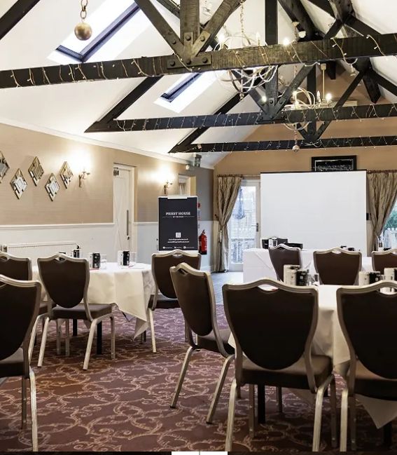 A conference or meeting room set up with round tables, chairs, and a projection screen under exposed beams with chandeliers.