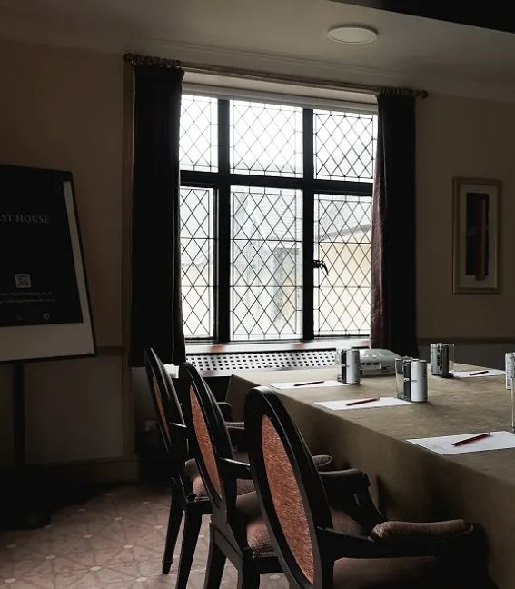 Meeting room with a large table, chairs, and meeting supplies set up near a window with lattice-style glass.