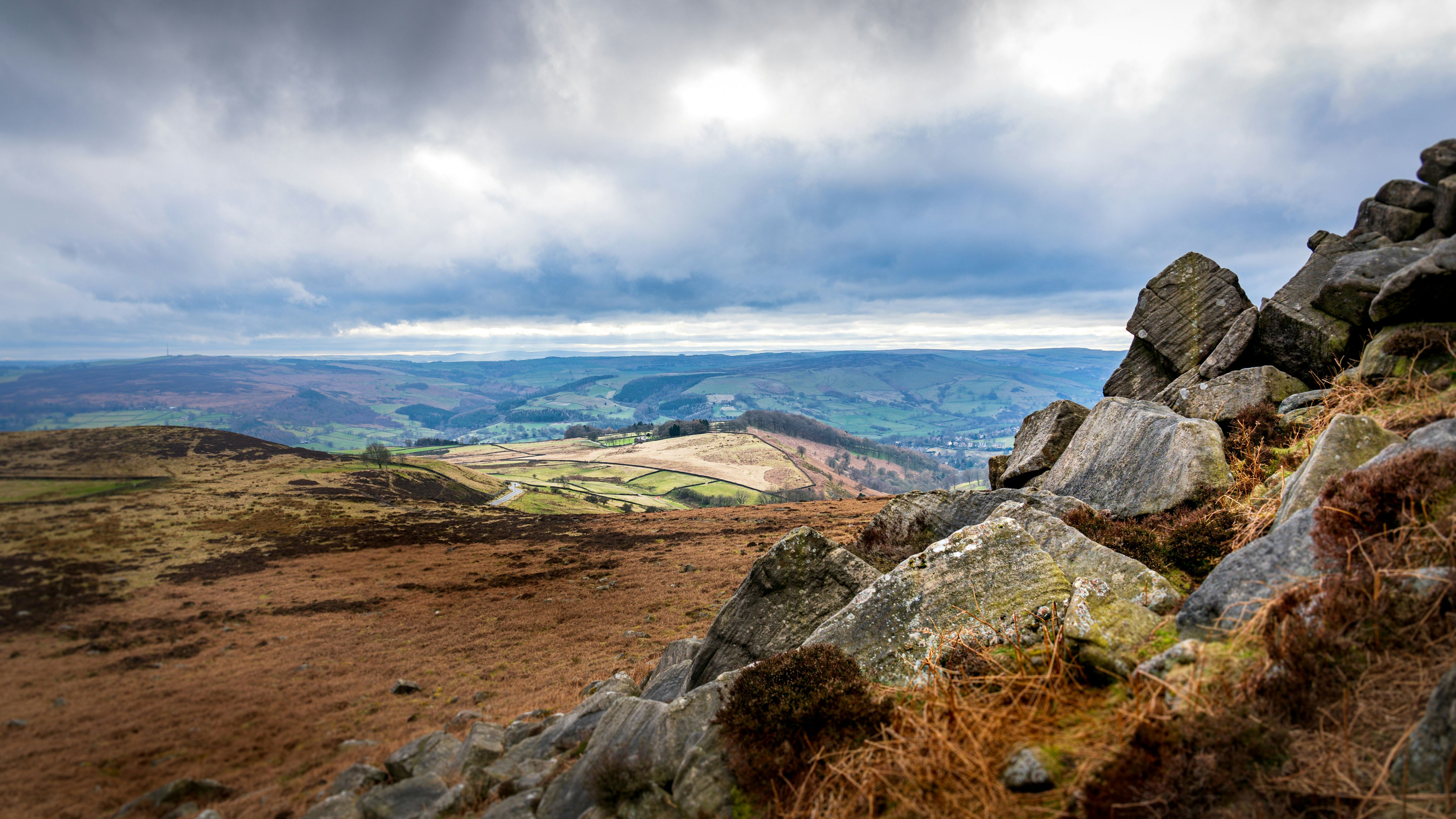 Rocky hillside overlooking a patchwork of fields and rolling hills under a cloudy sky