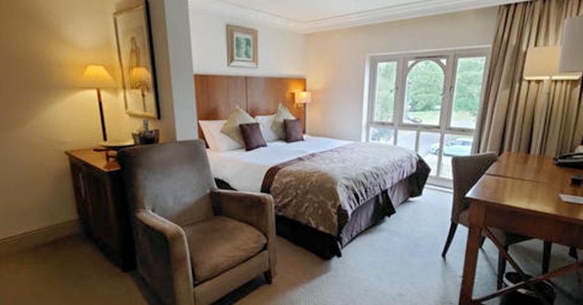 Well-furnished hotel room with a double bed, armchair, desk, and large window.