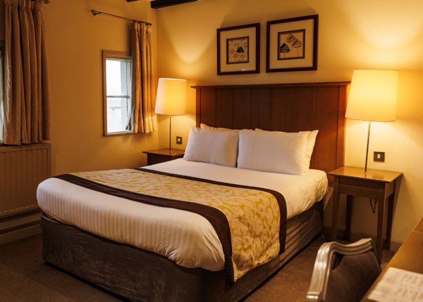 Cozy hotel room with double bed, wooden headboard, two bedside tables with lamps, and framed art above the bed