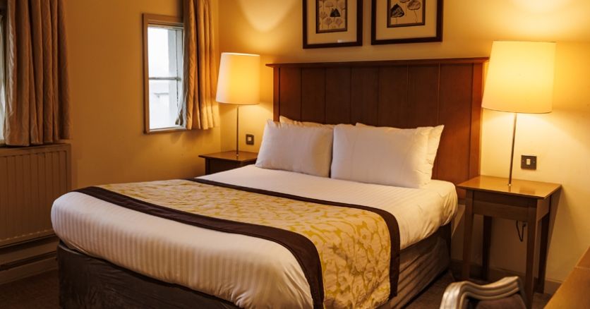 Cozy hotel room with double bed, wooden headboard, two bedside tables with lamps, and framed art above the bed