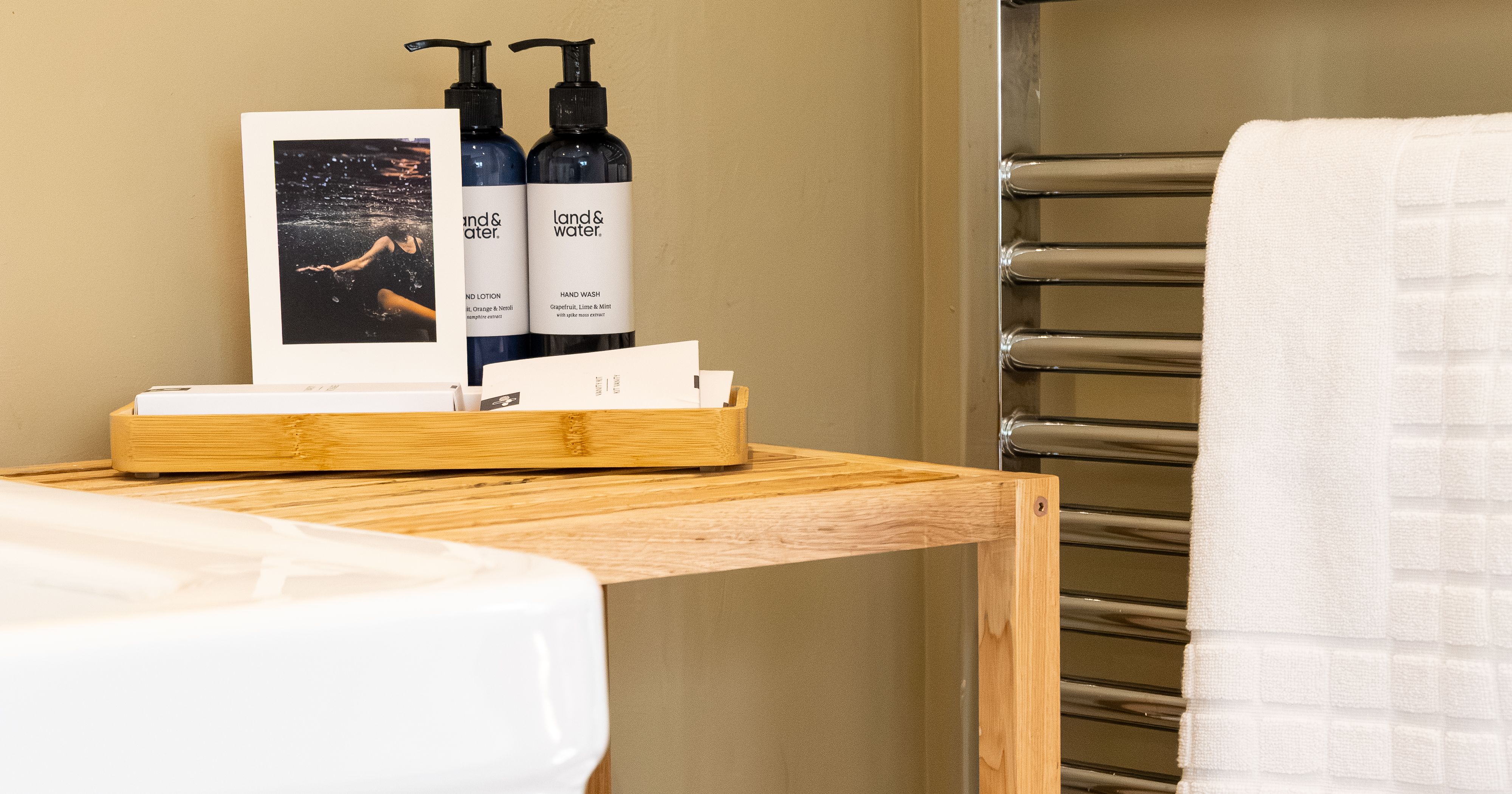 Bathroom shelf with rolled white towels, toiletries, and a towel rack with hanging towels.