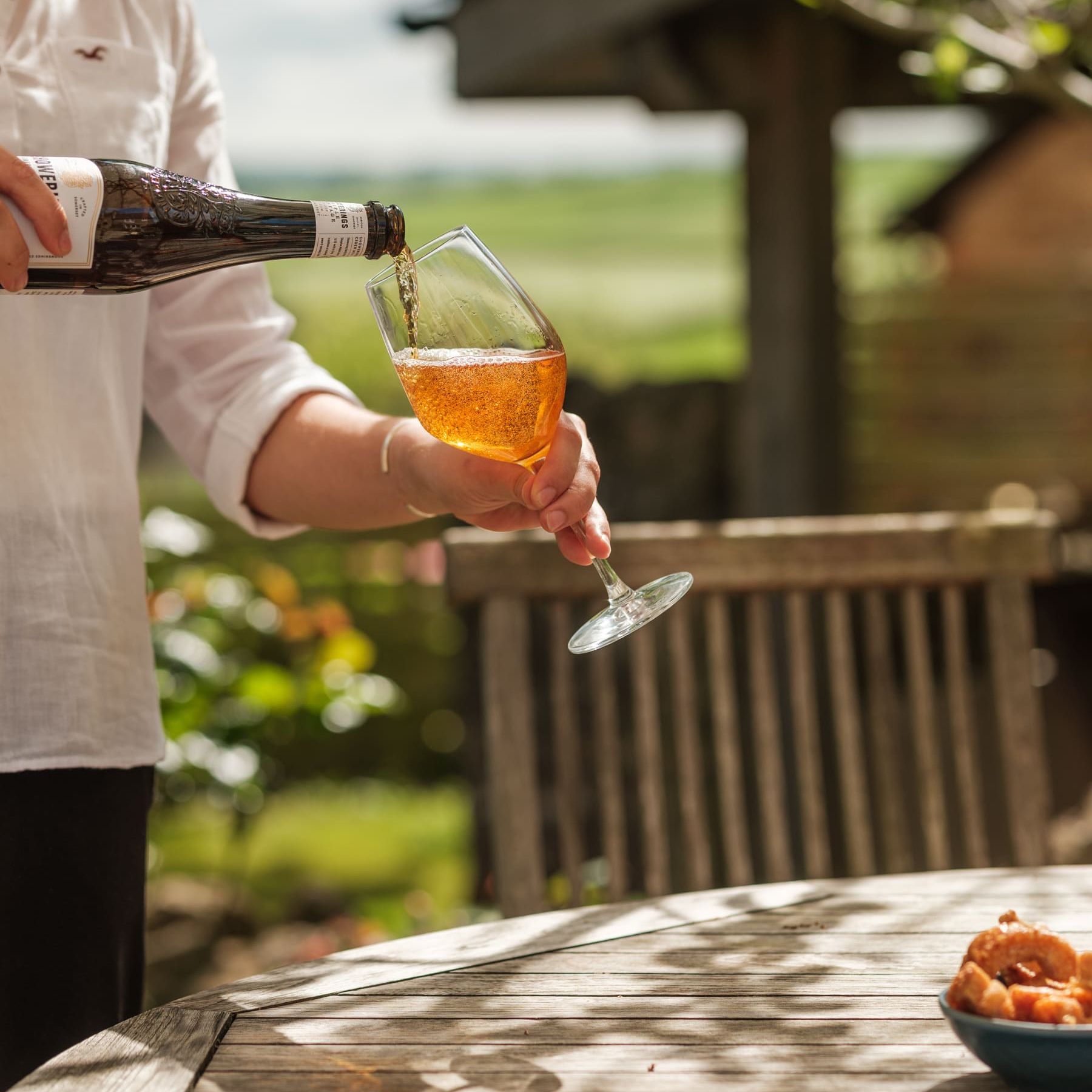 Person pouring cider into a wine glass outdoors on a sunny day