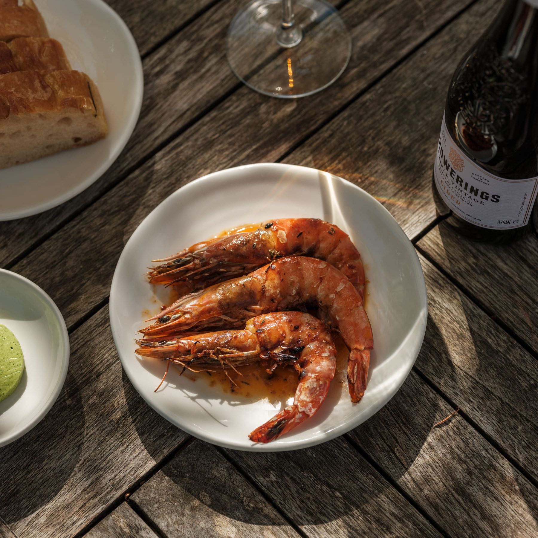 Plate of cooked shrimp with a glass of wine, bread, and a bottle on a wooden table