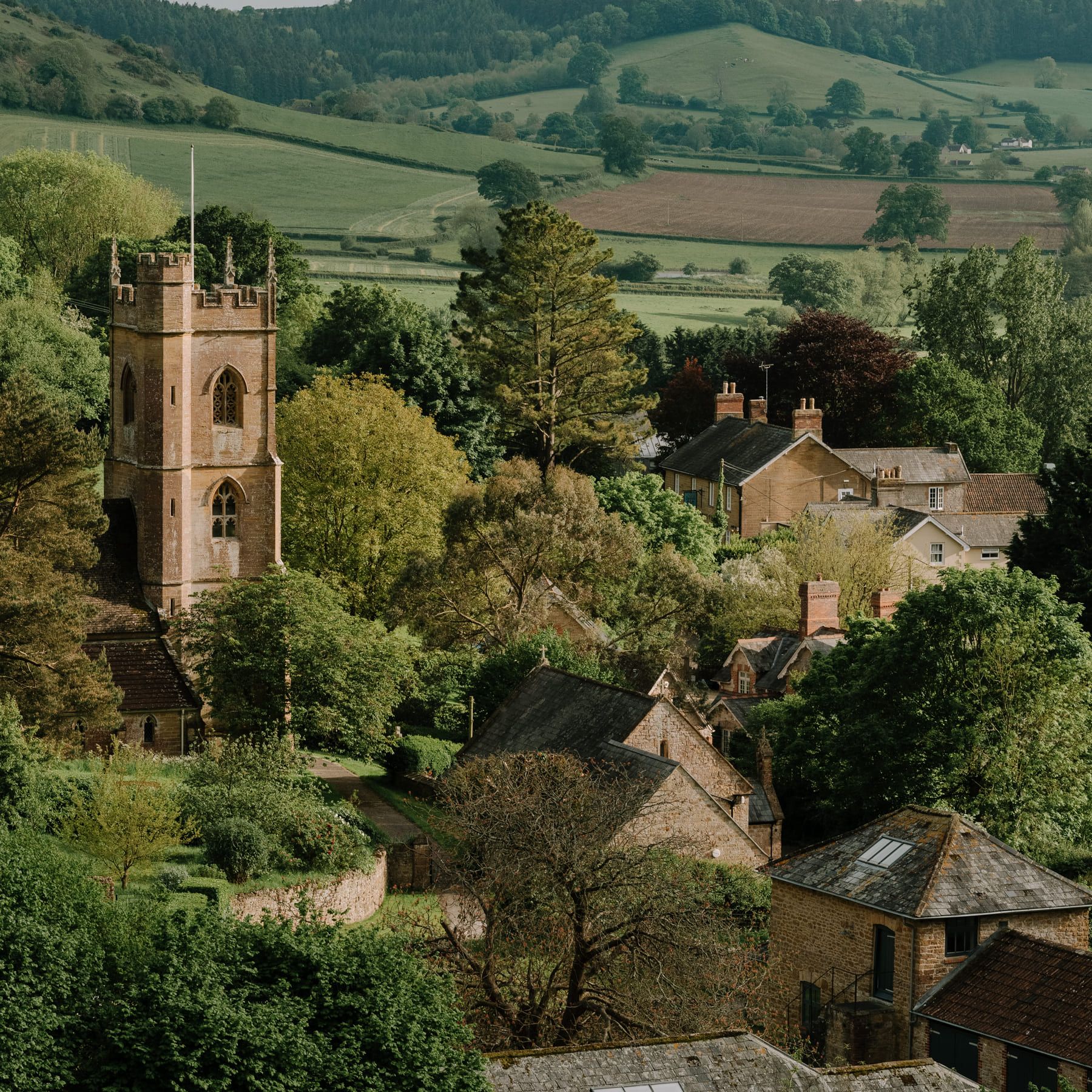 Picturesque English countryside village with a stone church tower and rolling green hills.