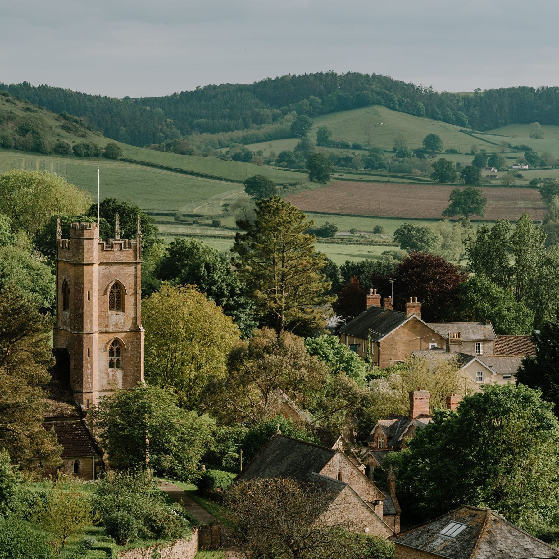 Picturesque English countryside village with a stone church tower and rolling green hills.