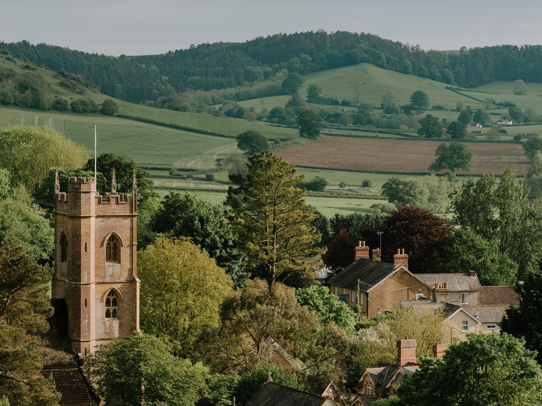Picturesque English countryside village with a stone church tower and rolling green hills.