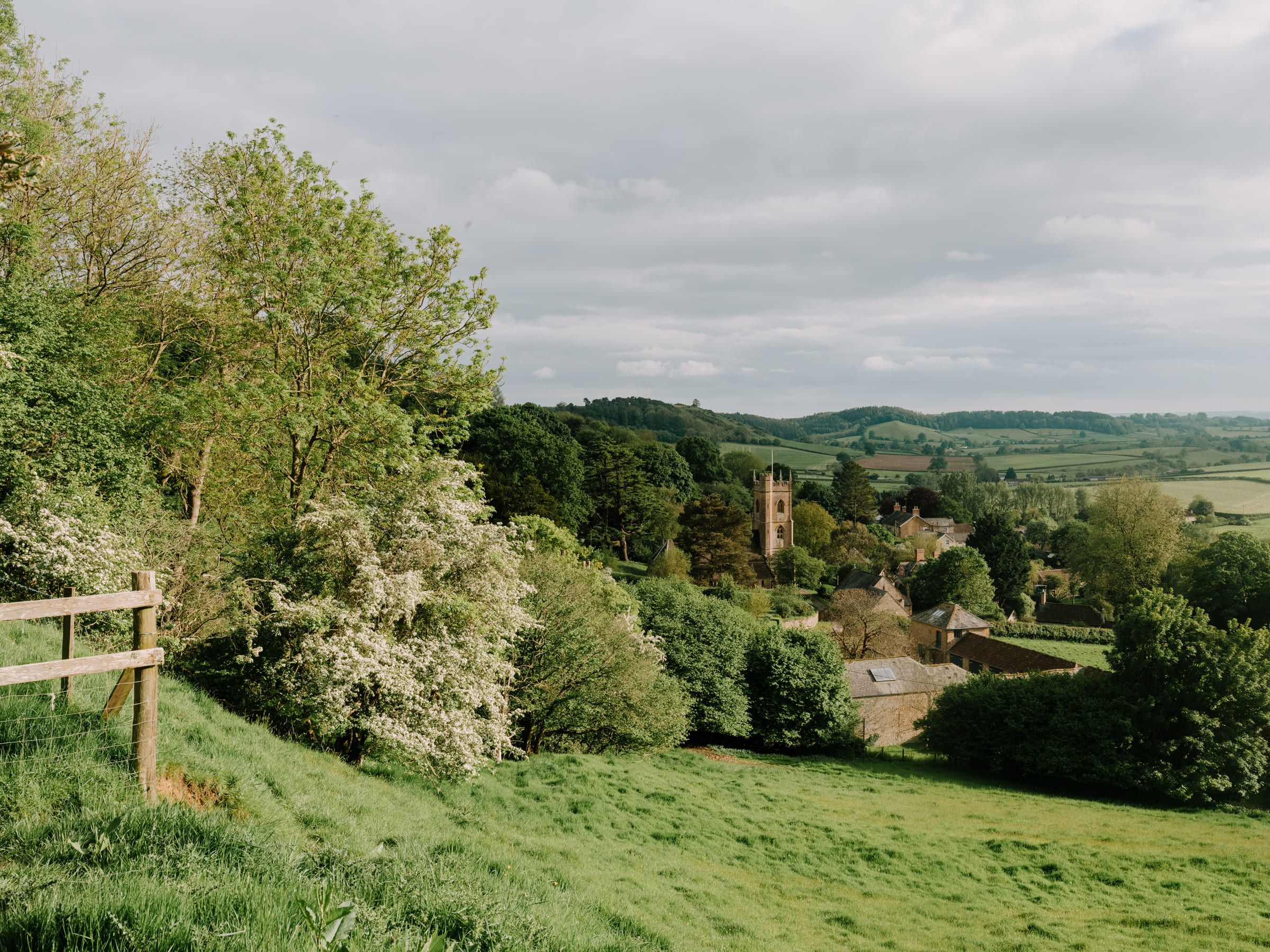 A picturesque rural village with a church tower surrounded by lush green fields and trees.