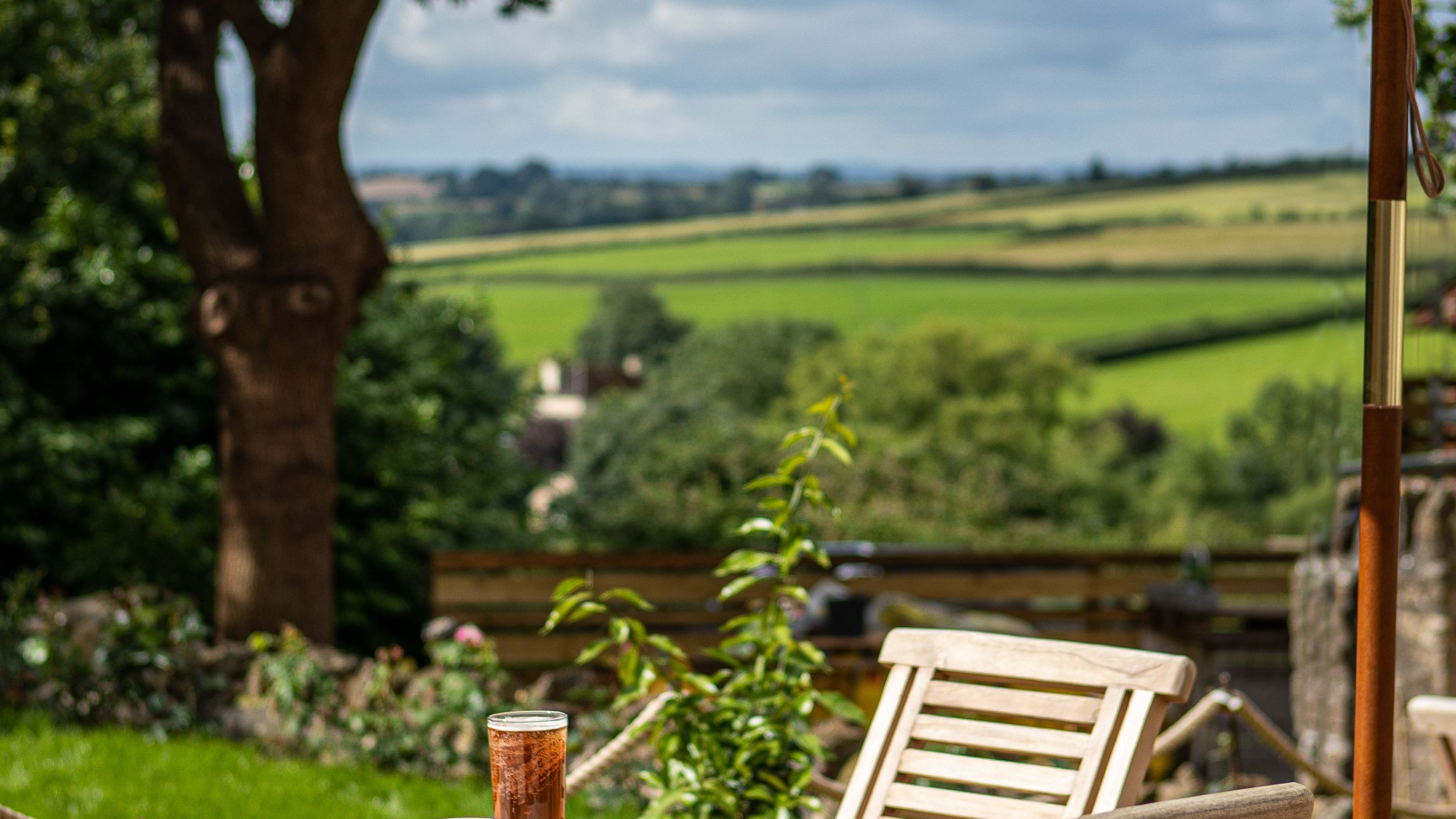 Outdoor seating with a drink on a table overlooking a green countryside landscape