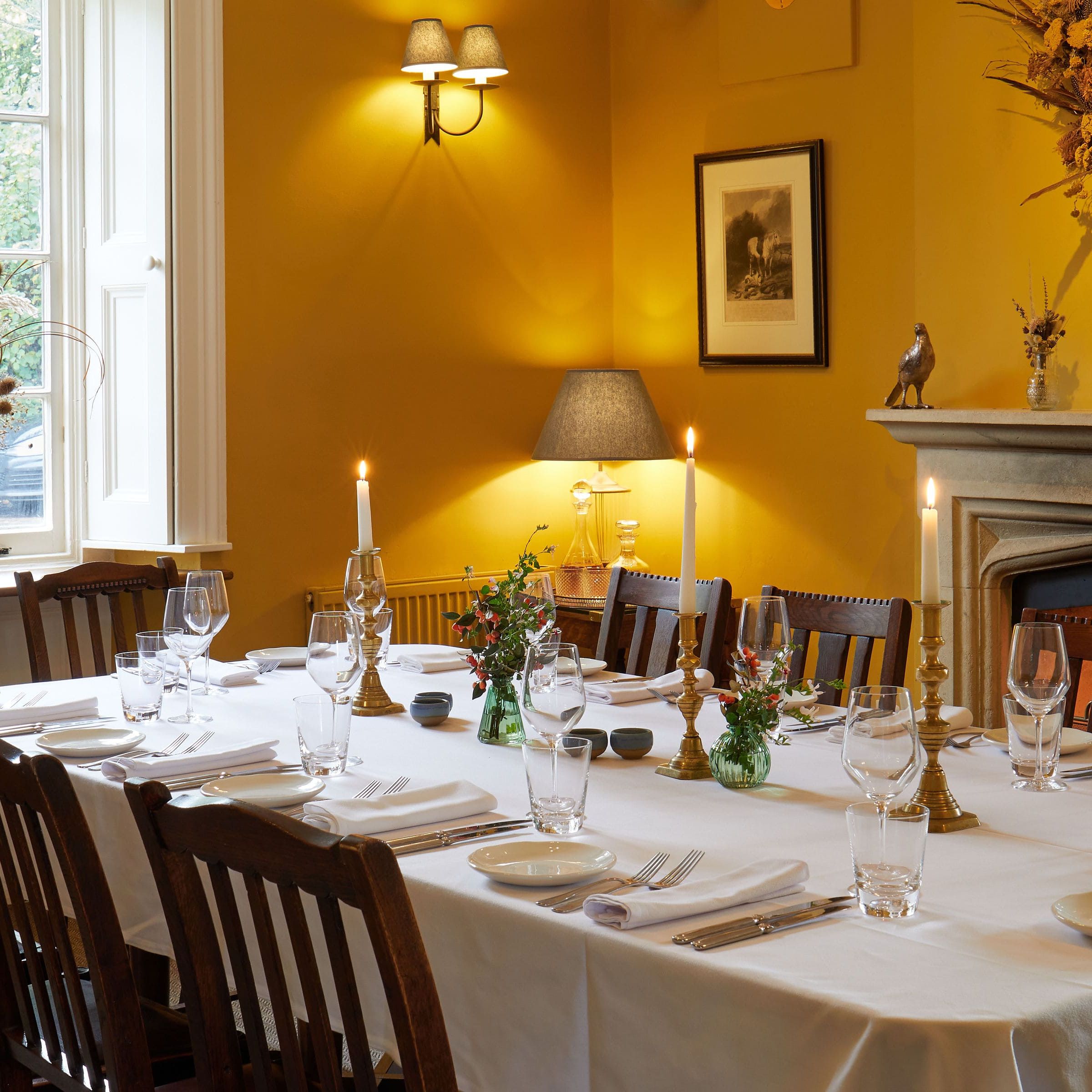 Elegant dining room with a set table, lit candles, and yellow walls.