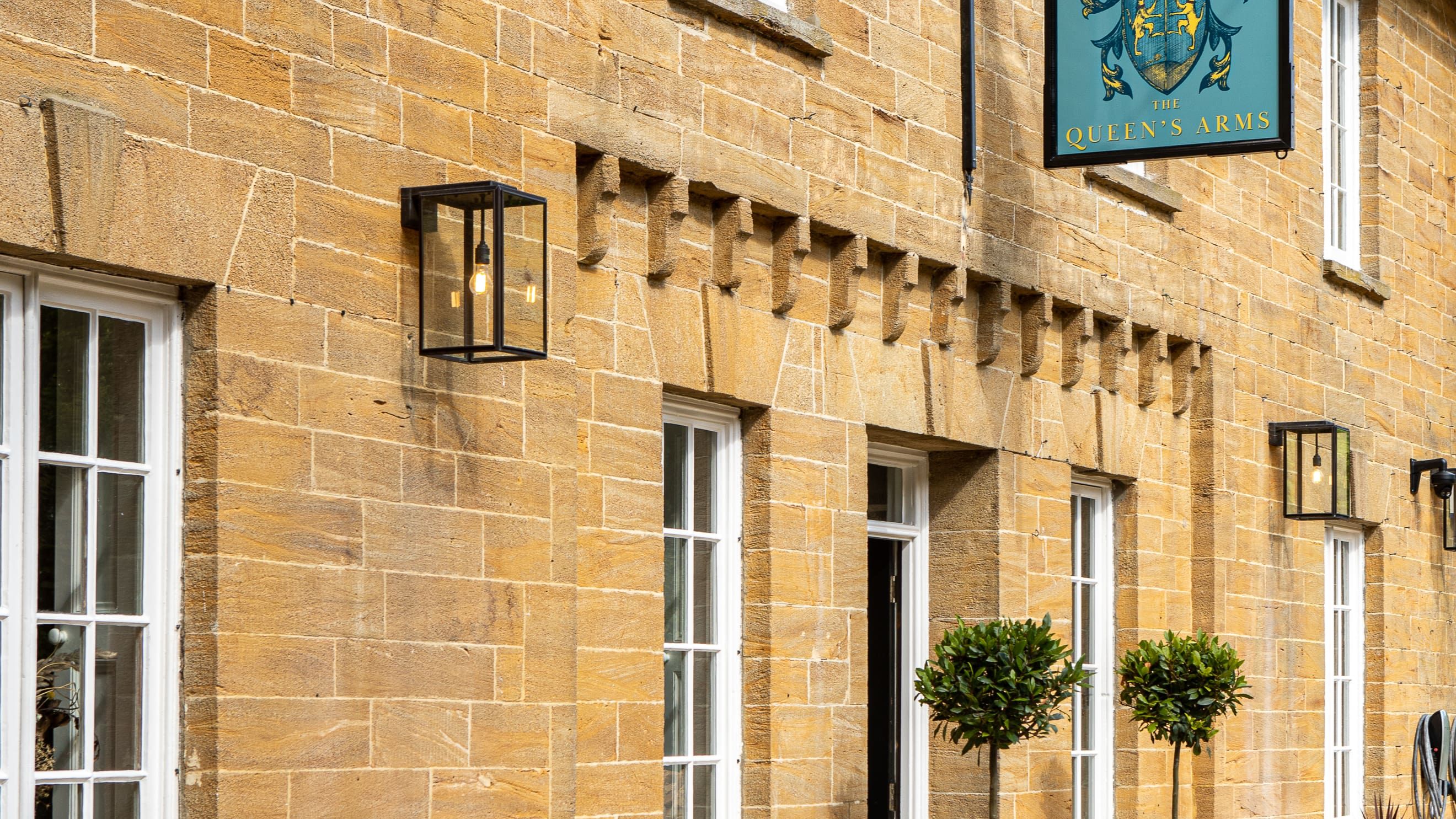 Exterior of The Queen's Arms, a traditional stone building with white windows and flower baskets.