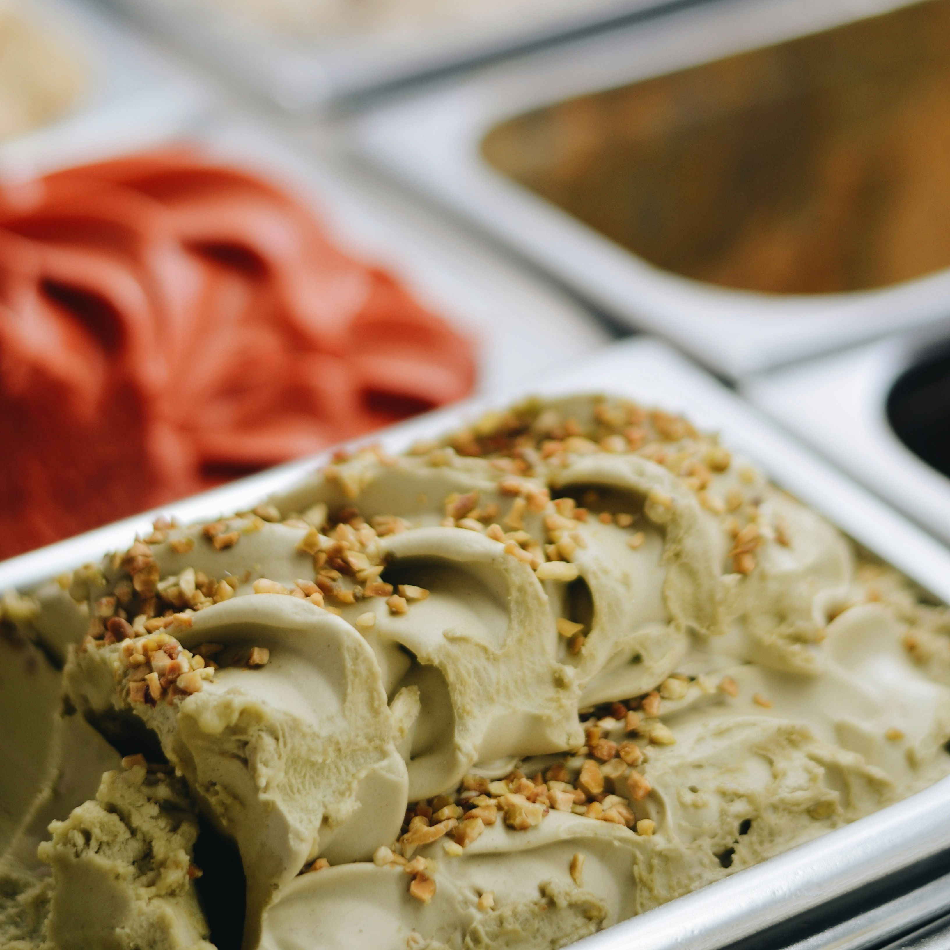 Assorted trays of gelato with various flavors, including pistachio with chopped nuts on top.