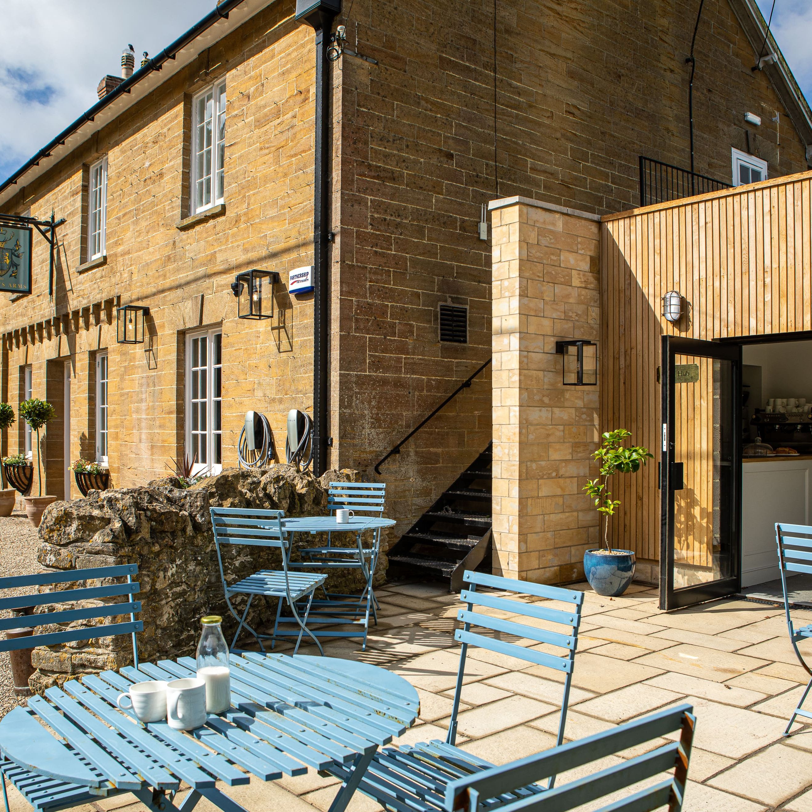 Outdoor seating area of a café with blue tables and chairs in front of a stone building