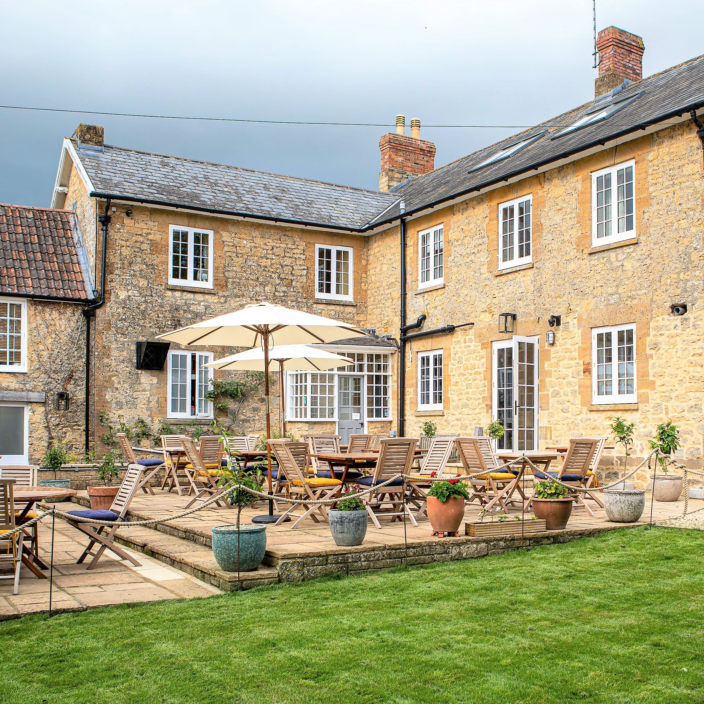 Outdoor seating area with wooden tables and chairs in front of a rustic stone building
