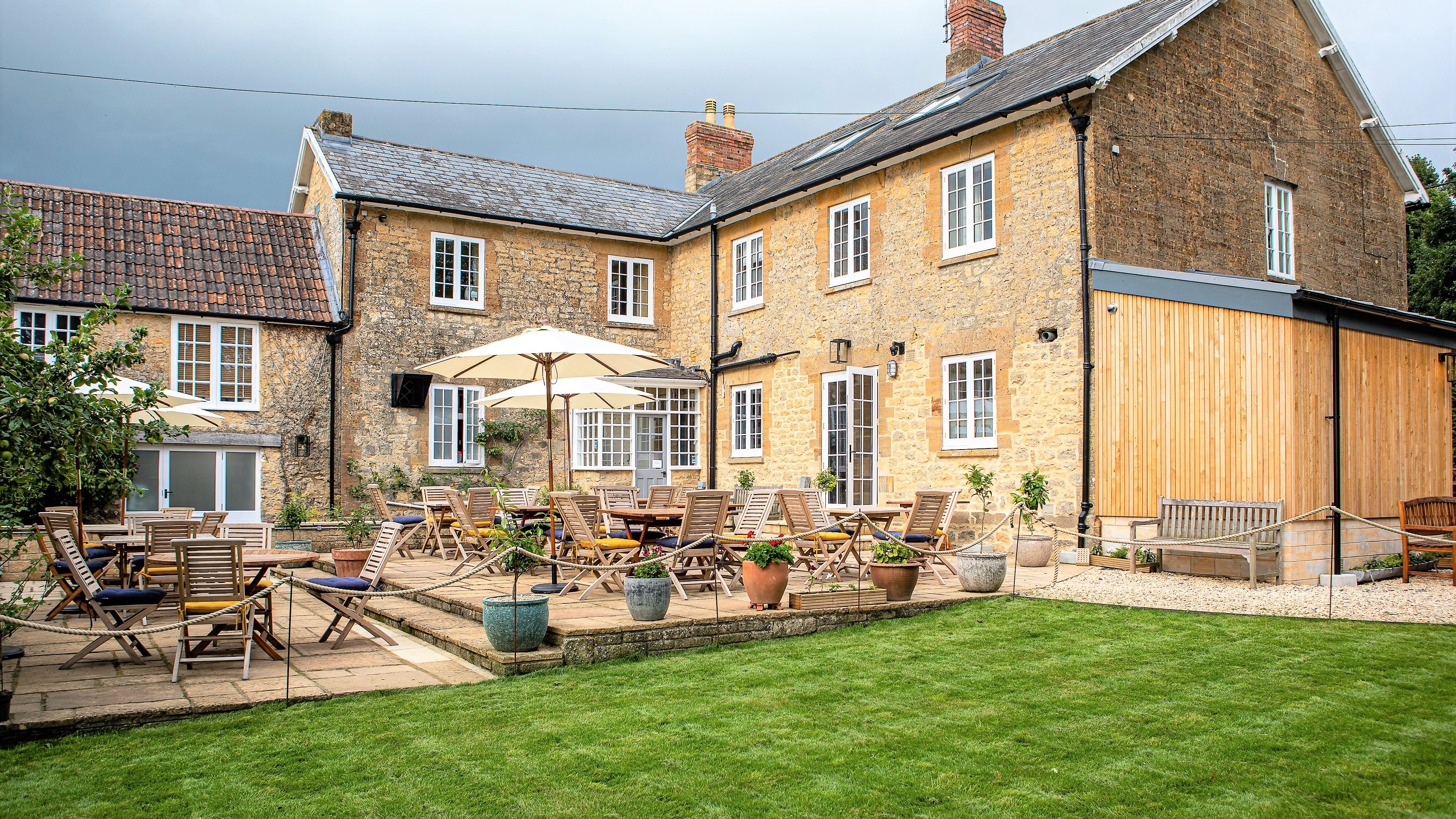 Outdoor seating area with wooden tables and chairs in front of a rustic stone building