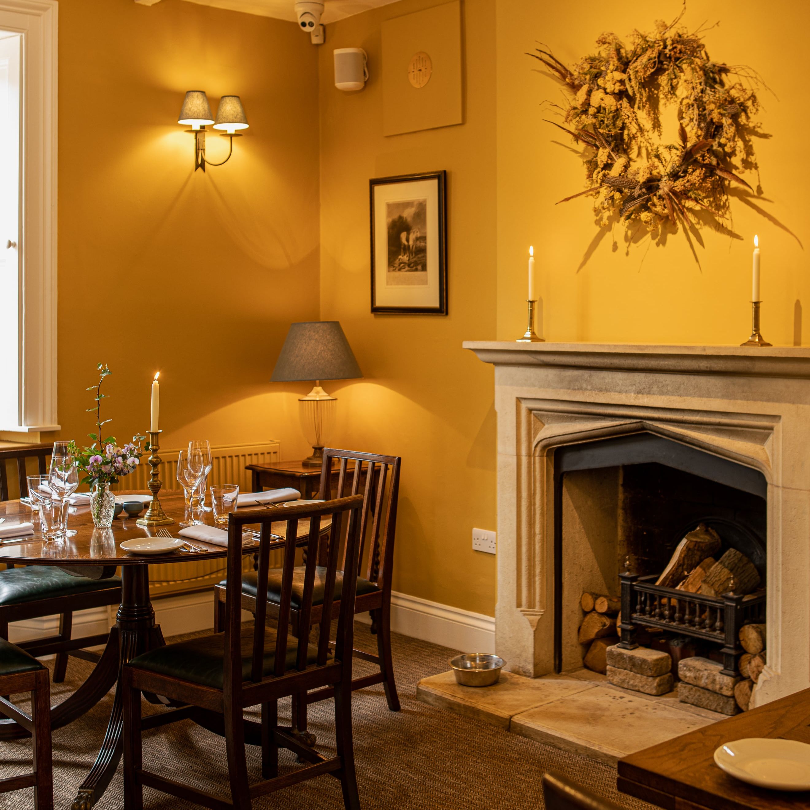 Cozy restaurant dining area with wooden chairs, set table, fireplace, and warm lighting.
