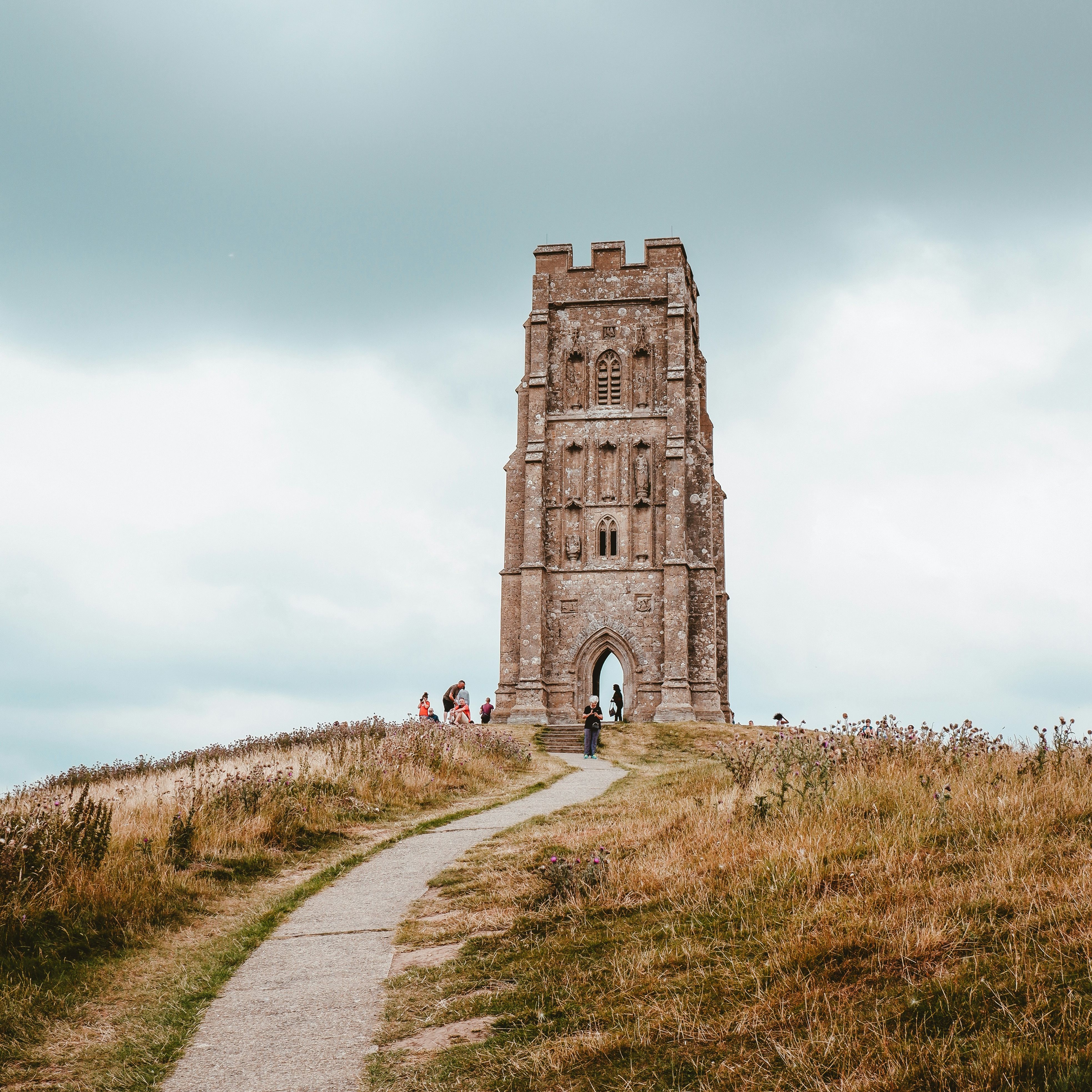 Tall stone tower on a grassy hill with a pathway leading up to it, under a cloudy sky