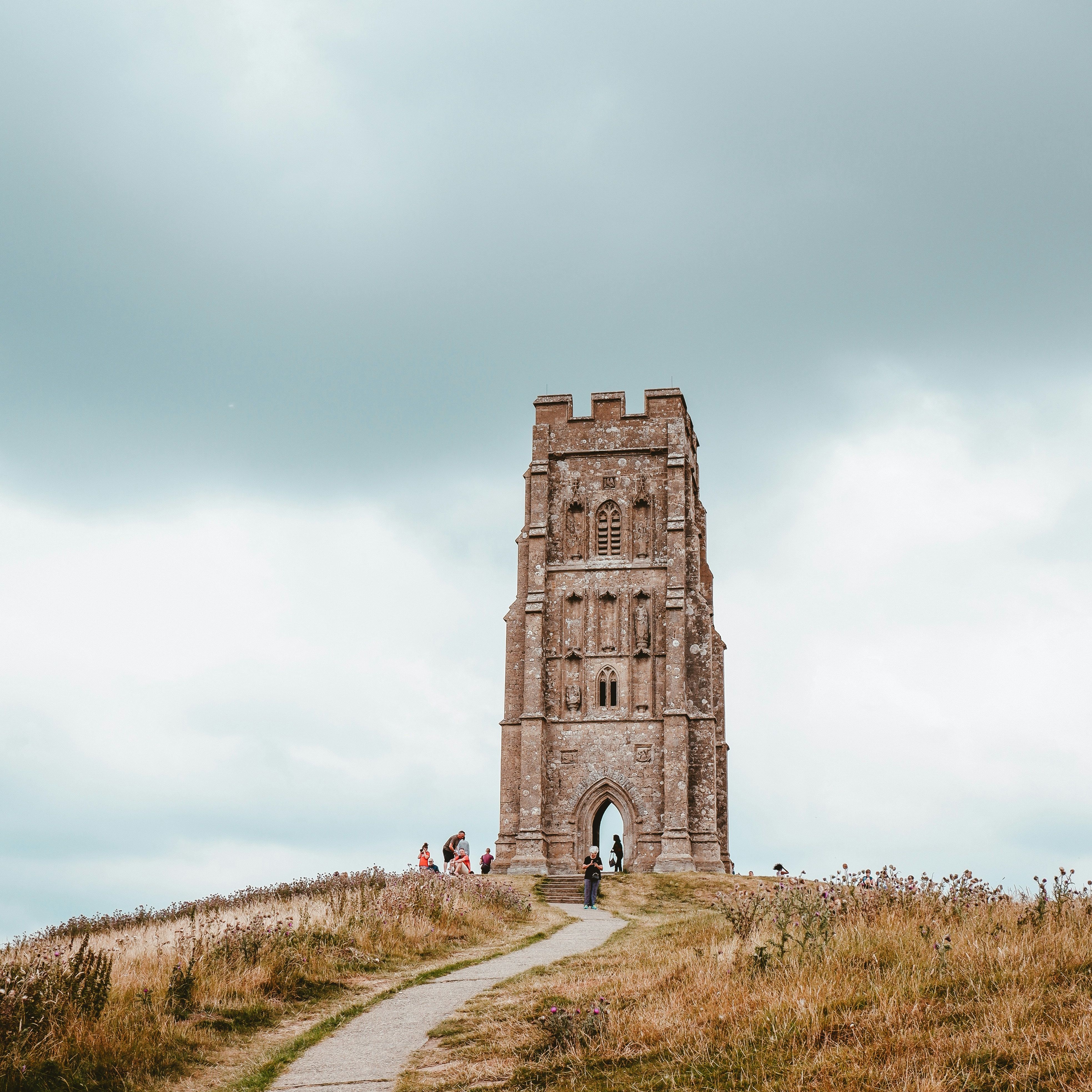 Tall stone tower on a grassy hill with a pathway leading up to it, under a cloudy sky