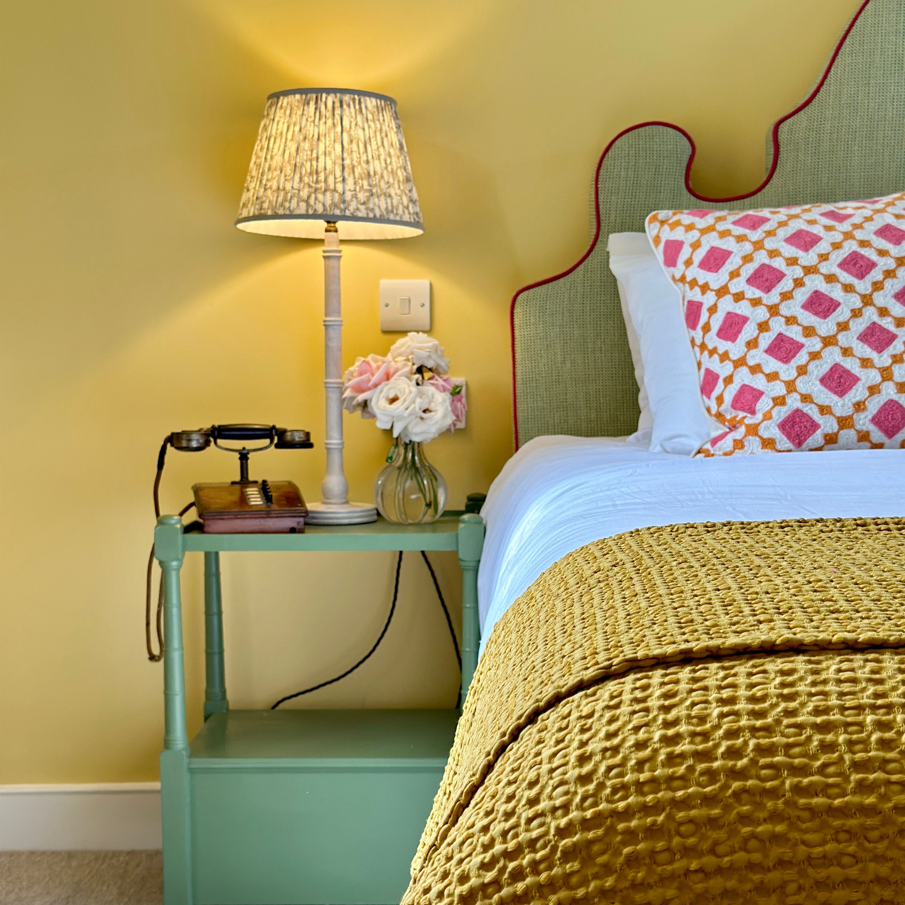 Cozy bedroom corner with a lamp, vintage telephone, flowers, and yellow bedding