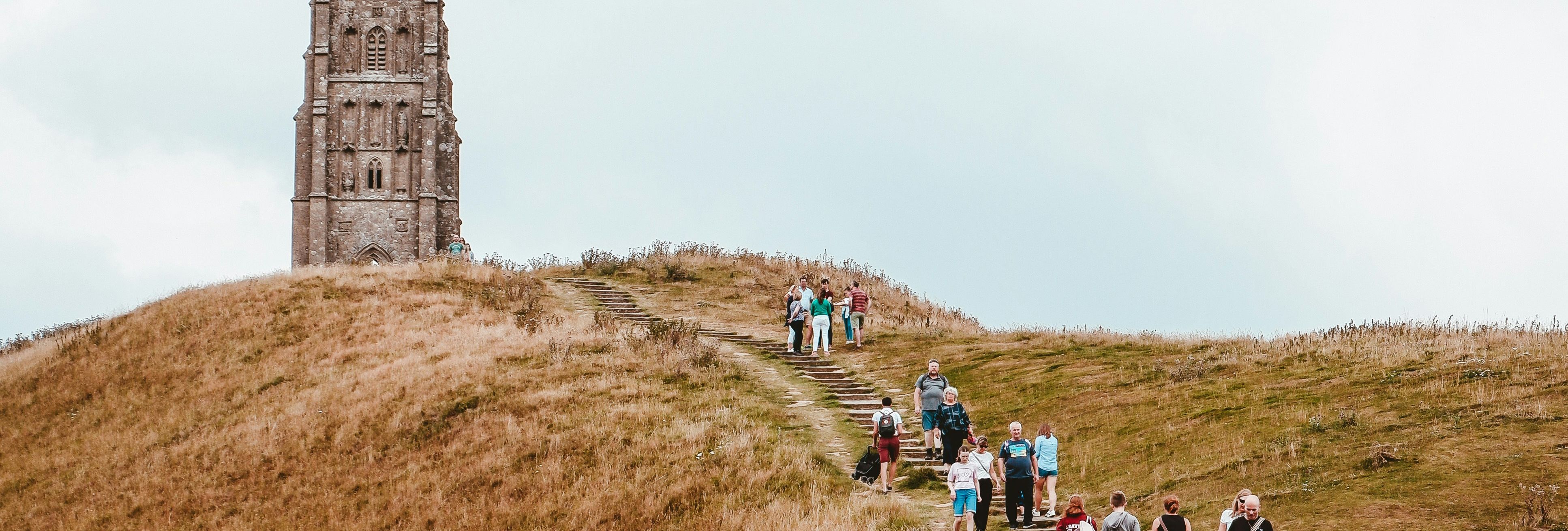 People walking up a grassy hill towards a historic stone tower