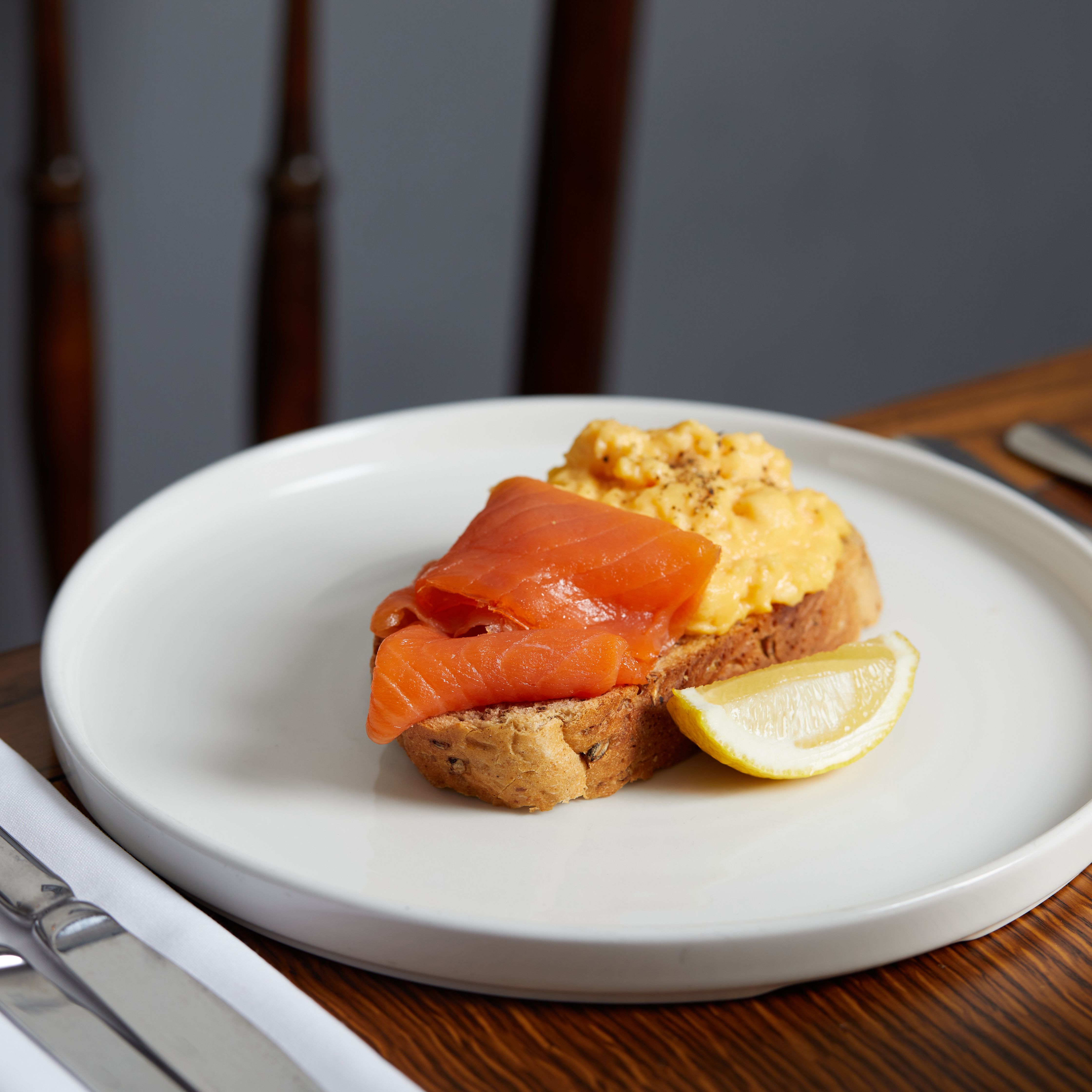 Open-faced sandwich with smoked salmon, scrambled eggs, and a lemon wedge on a white plate
