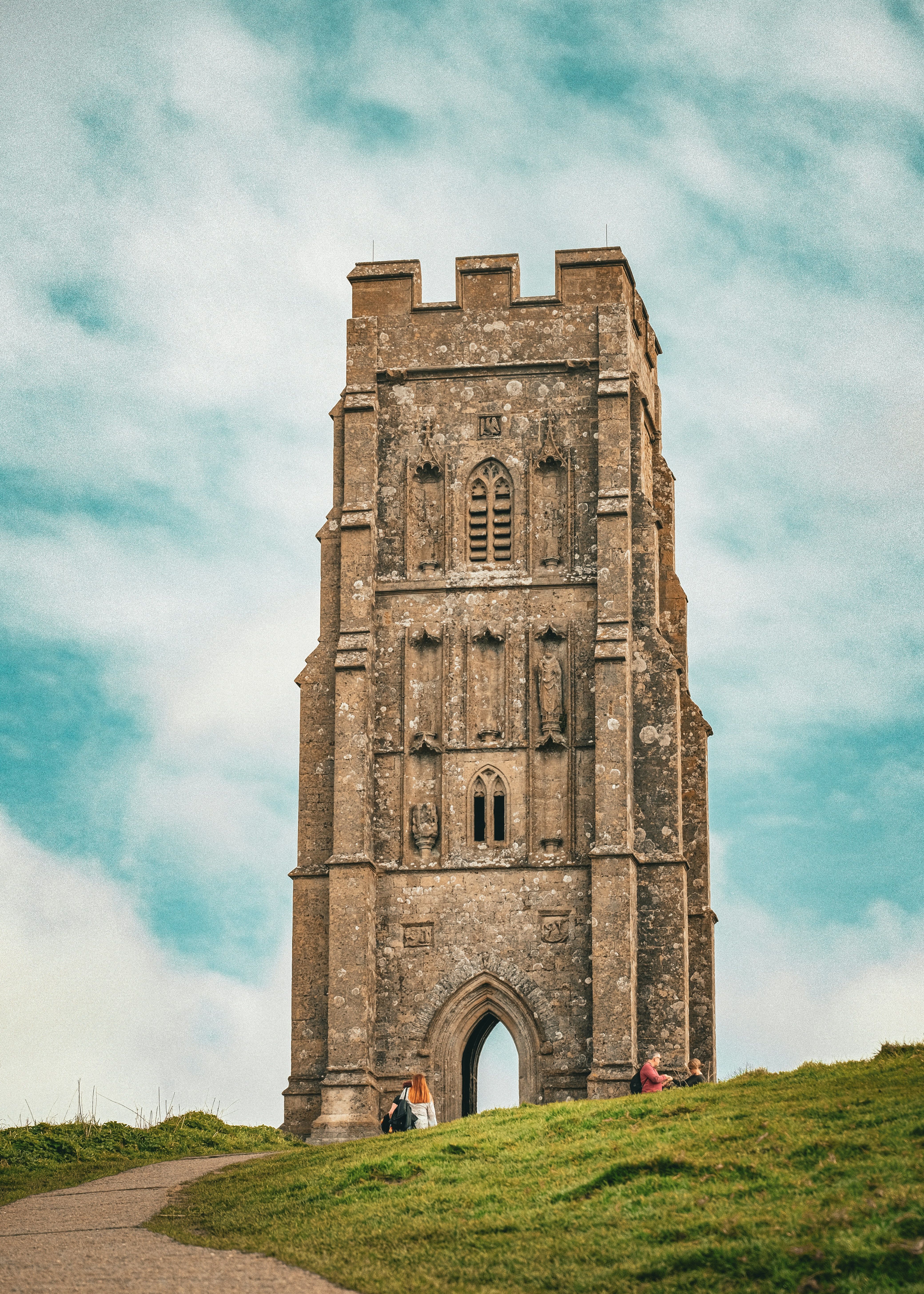 Ancient stone tower on a grassy hill with people nearby