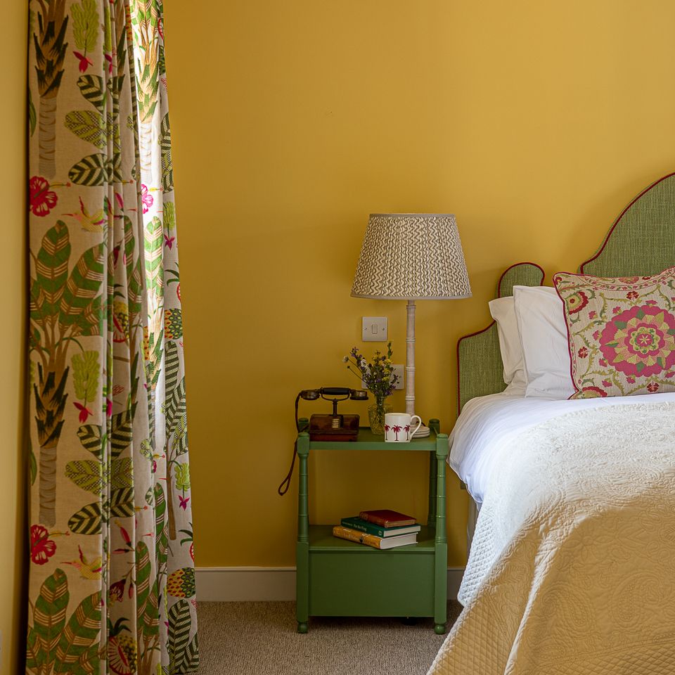 Cozy bedroom with yellow walls, floral curtains, bedside table, and vintage decor