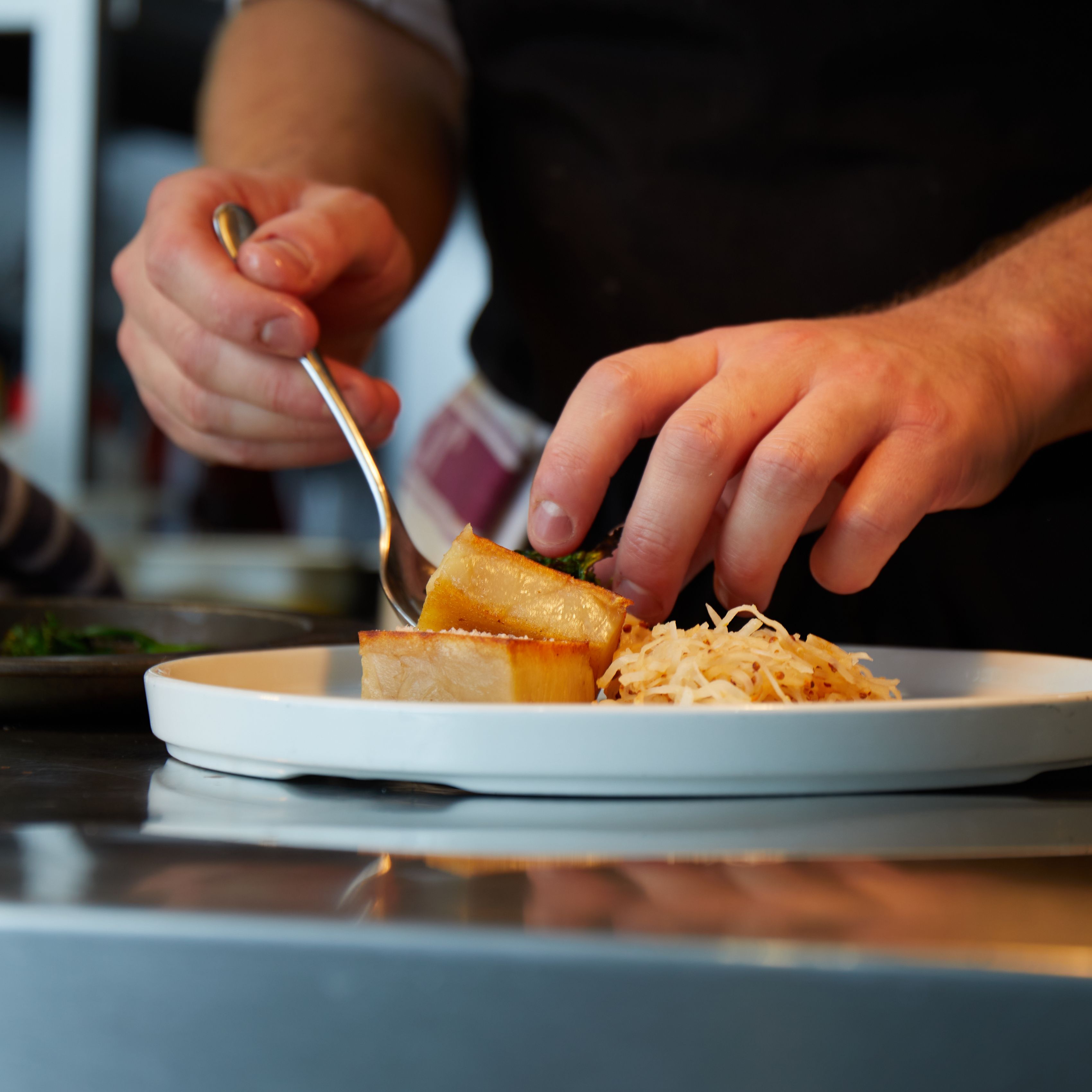 Chef arranging food on a white plate in a kitchen
