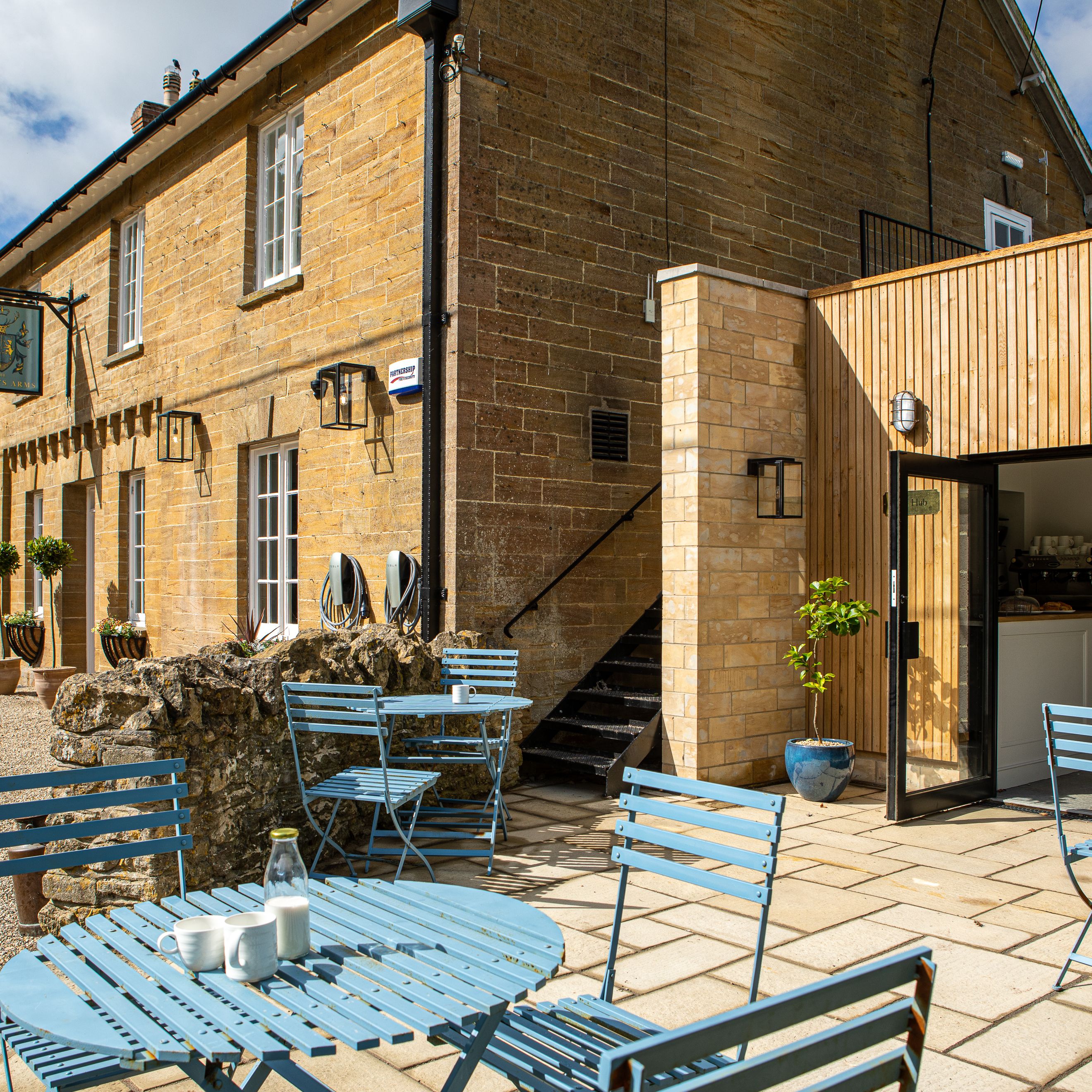 Outdoor seating area with blue tables and chairs outside a stone building and a modern wooden extension