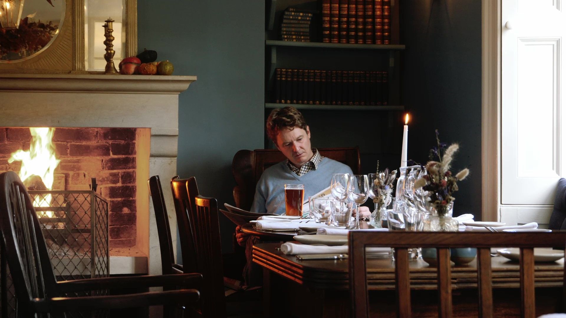 Man reading at a set dining table by a fireplace