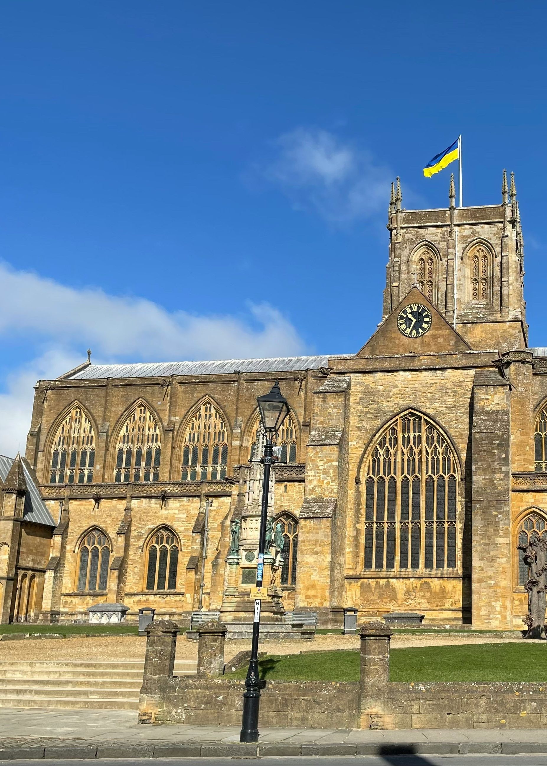 Historic stone church building with arched windows, a clock tower, and a blue and yellow flag on top, under a blue sky.